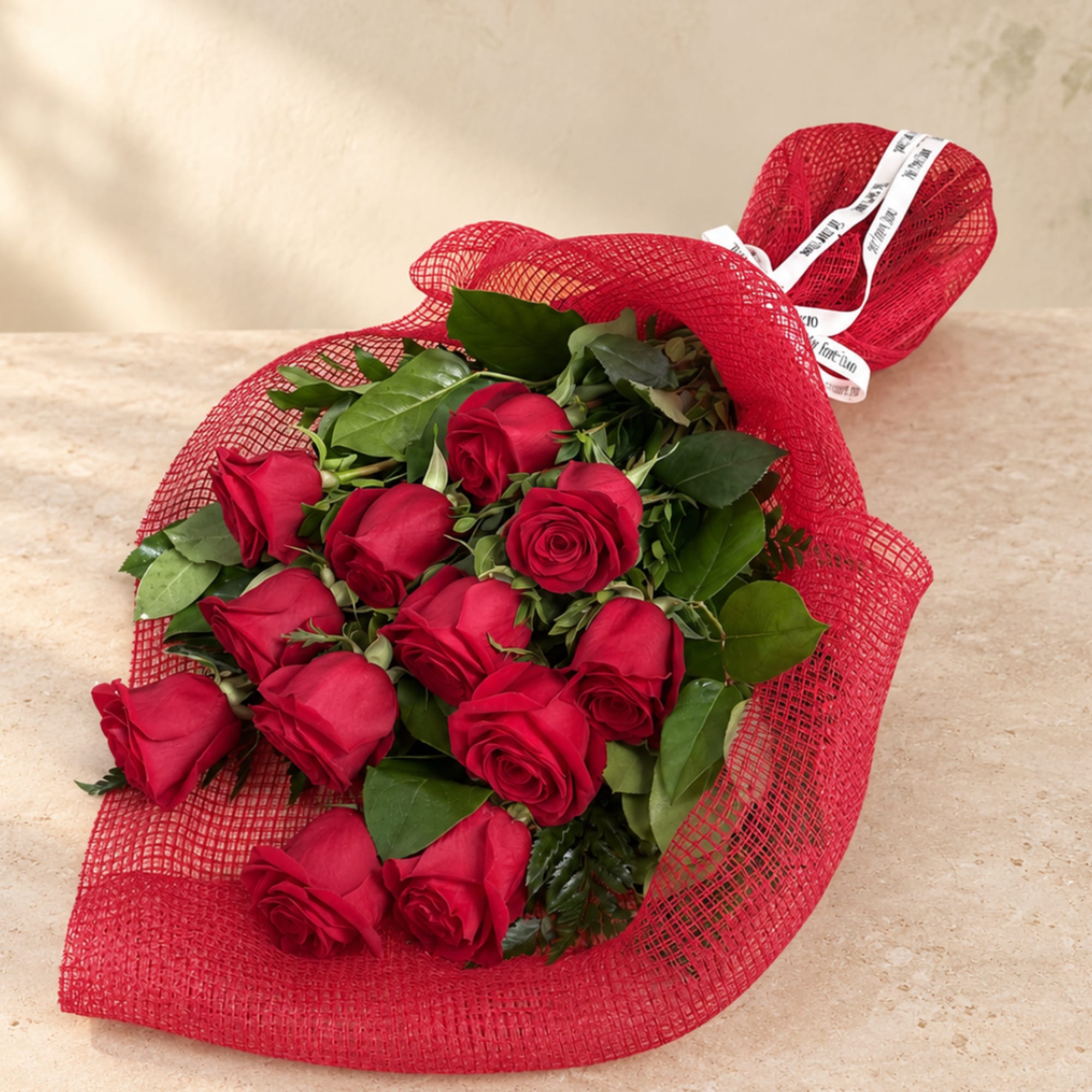 Bouquet of red roses wrapped in red mesh with a white ribbon
