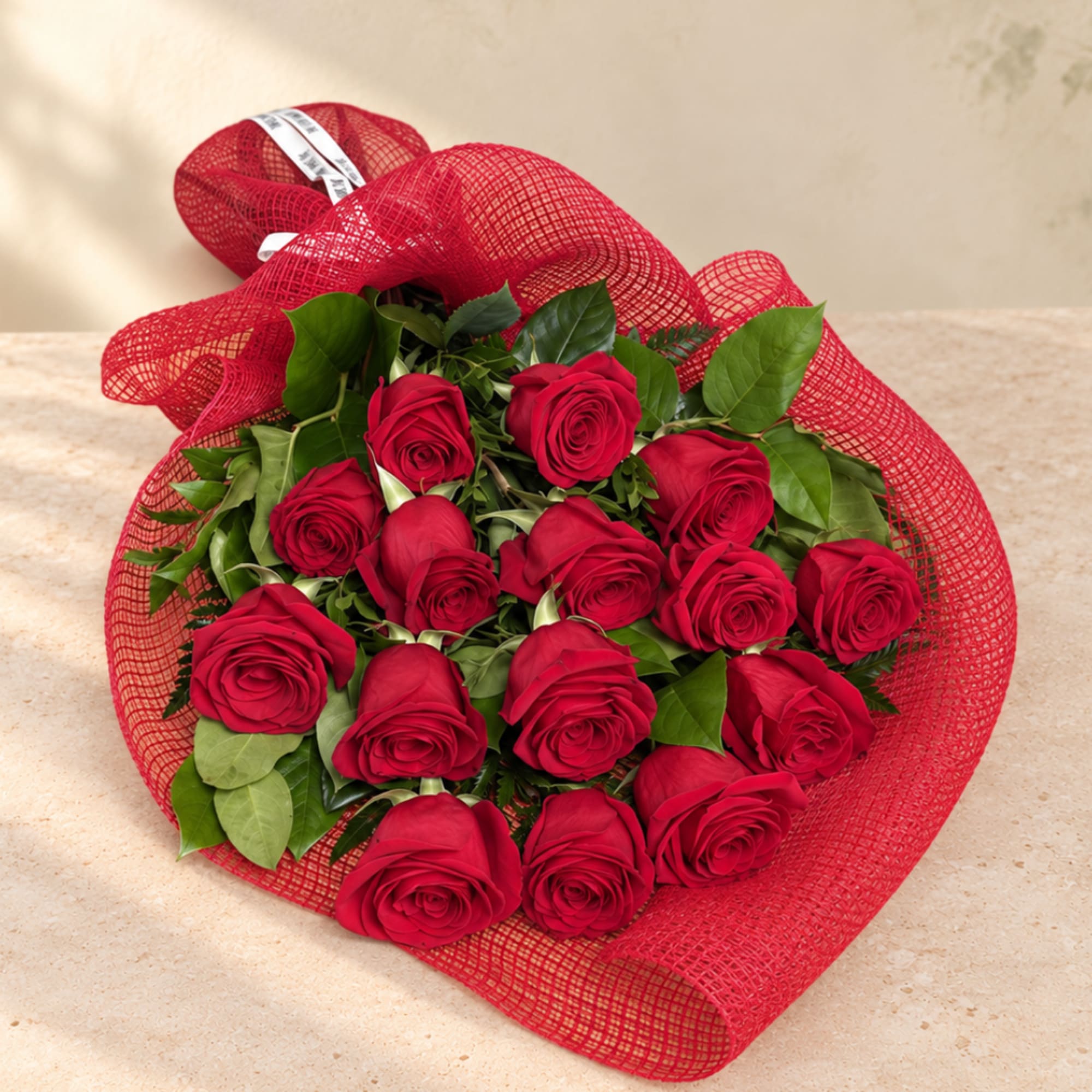 Bouquet of red roses wrapped in red mesh with green foliage