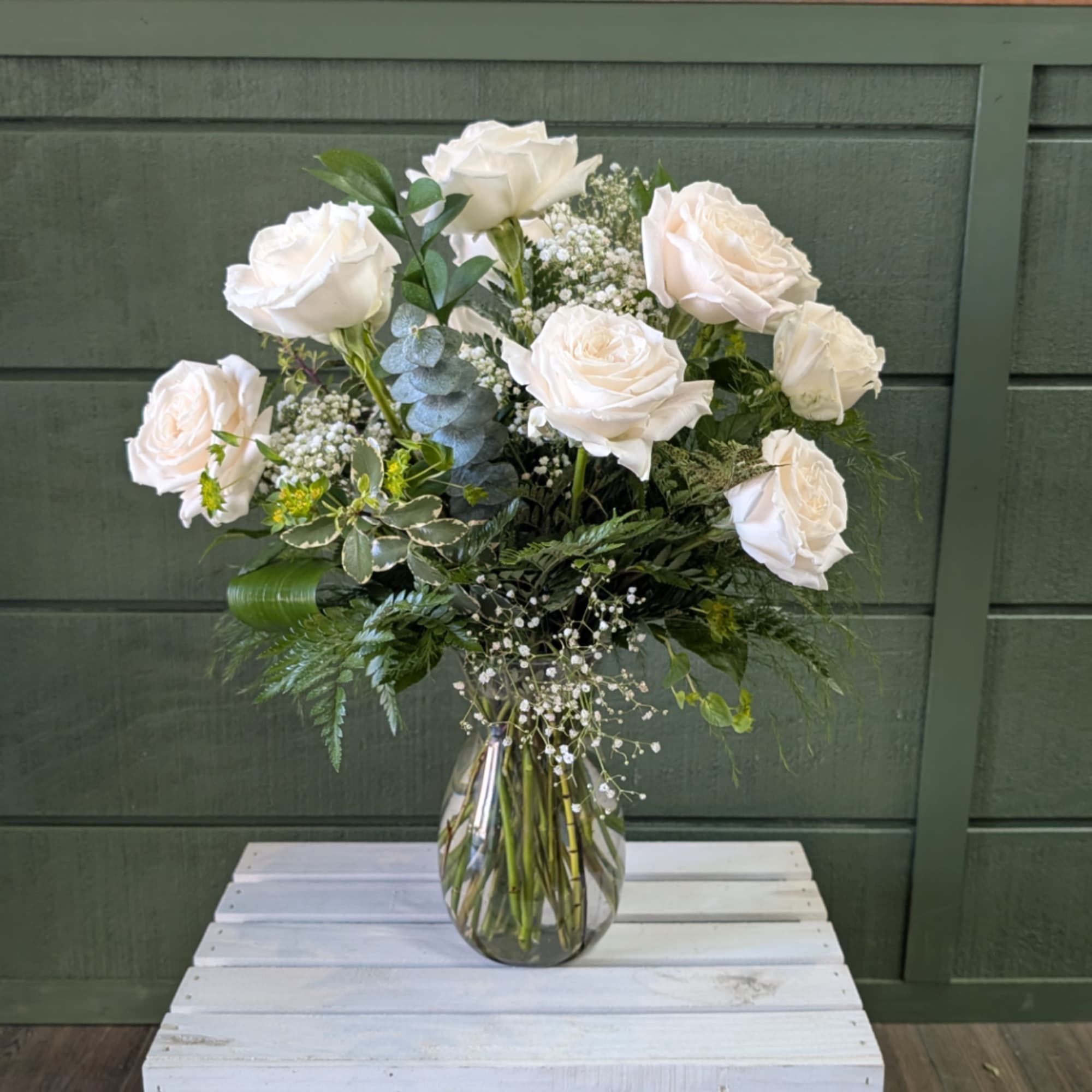 White roses arranged in a clear glass vase with mixed greenery
