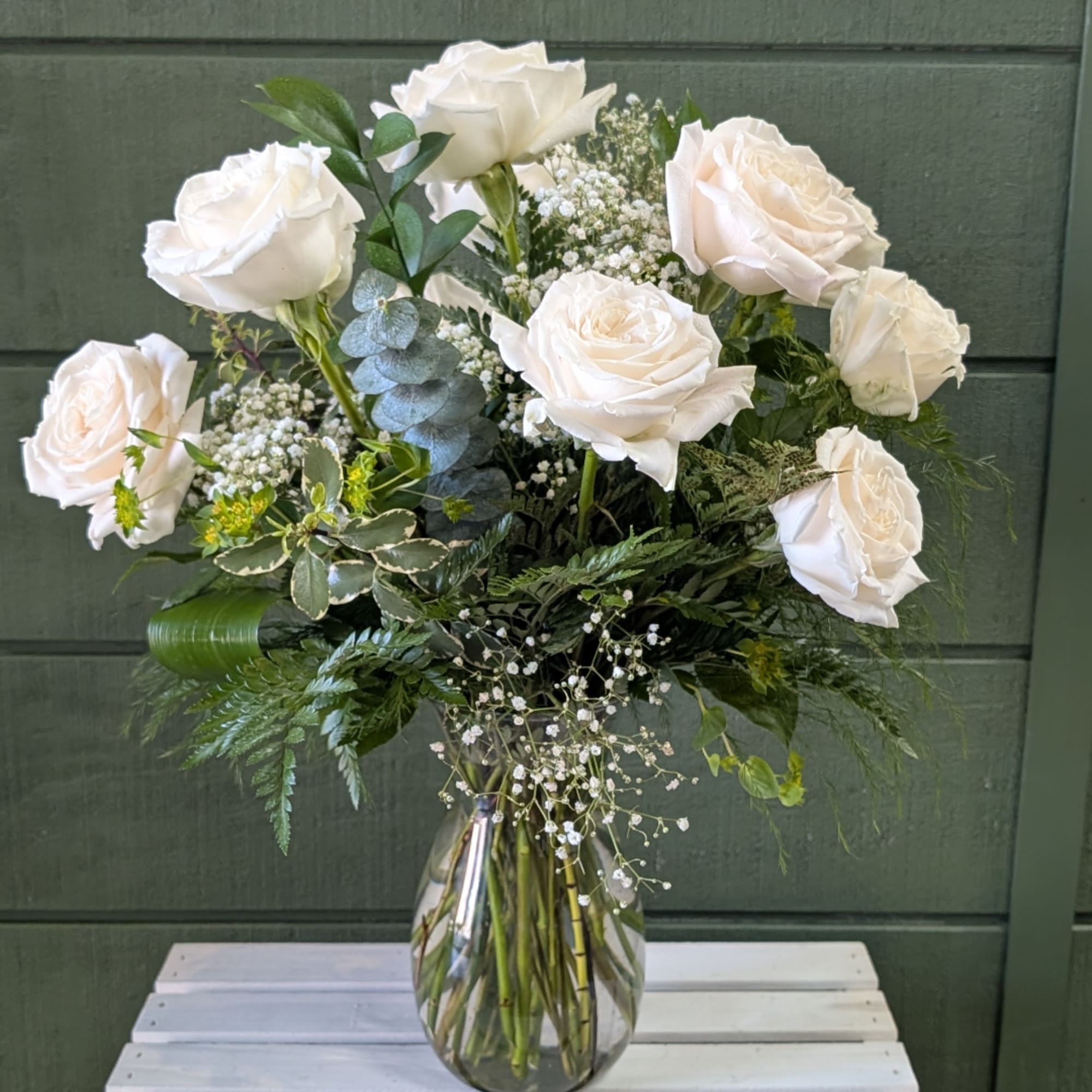White rose bouquet in a clear glass vase with mixed greenery