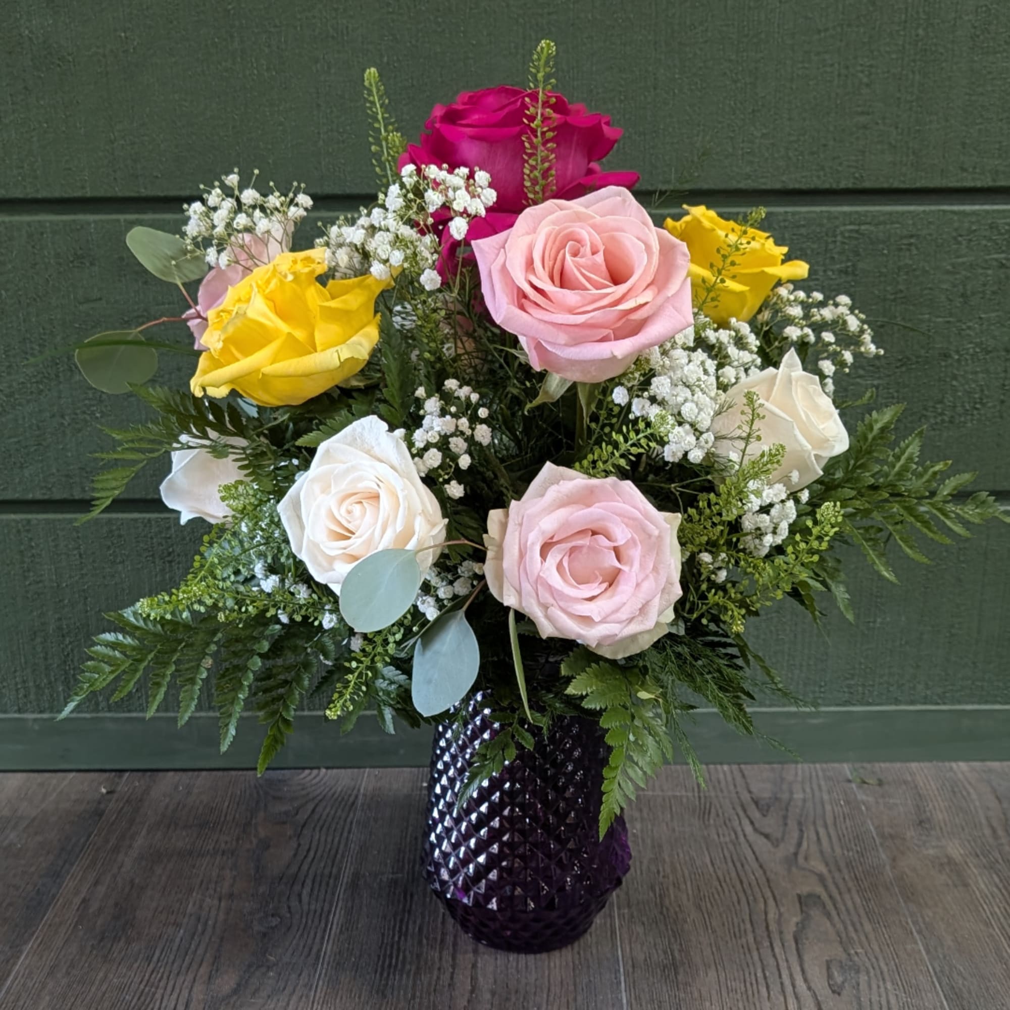 Mixed roses in pink, yellow, white, and magenta arranged in a dark vase