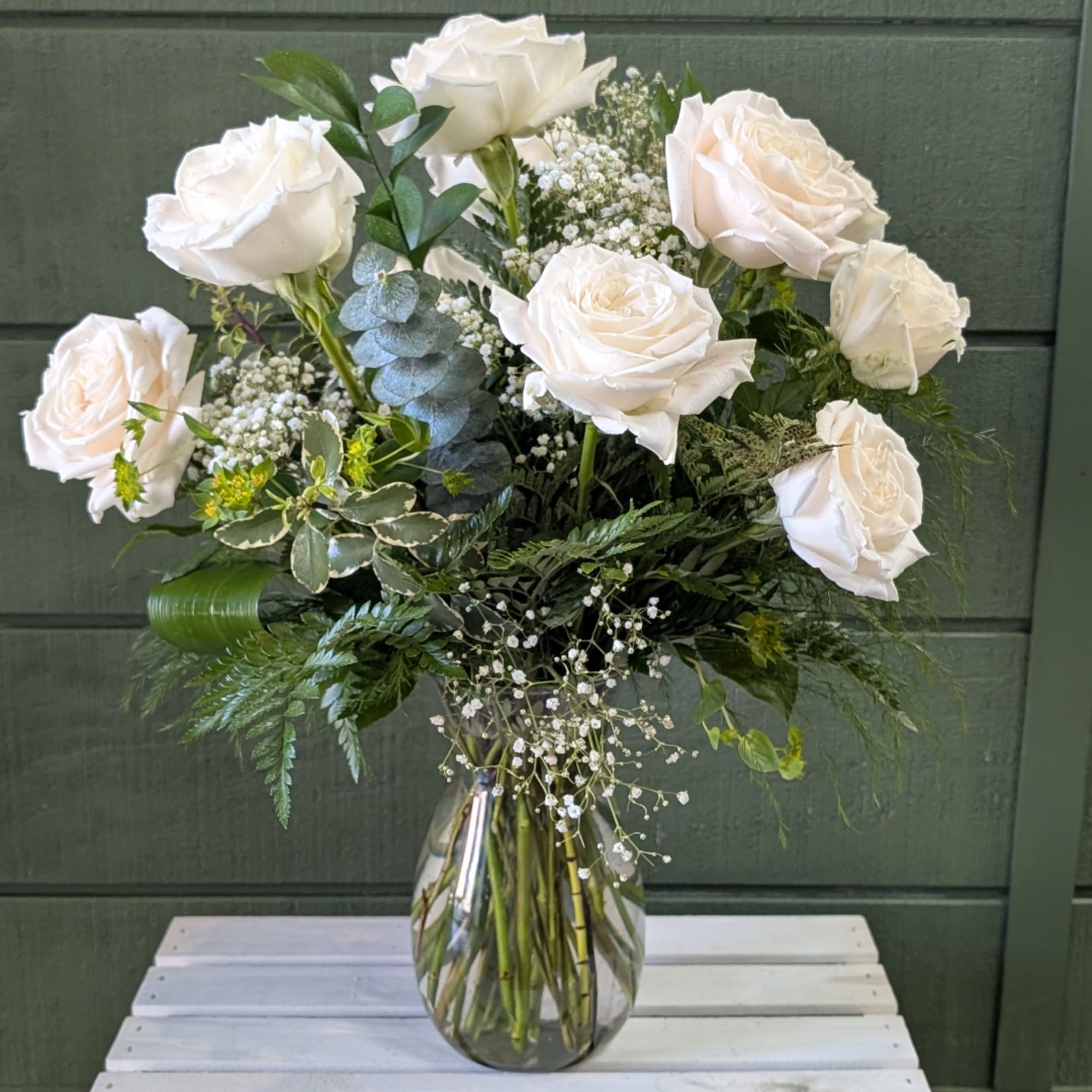 White roses arranged in a clear glass vase with mixed greenery