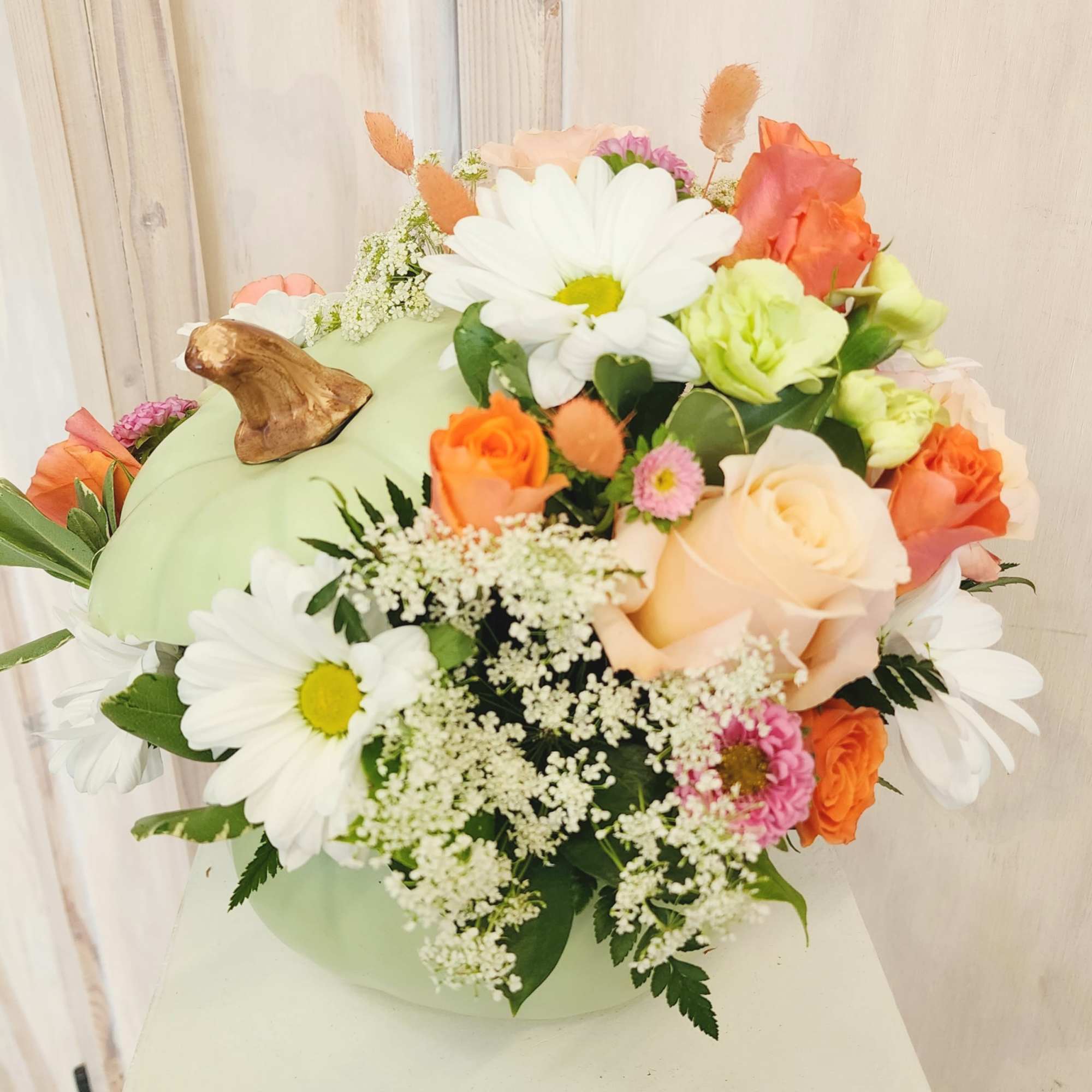 Mixed bouquet with daisies, roses, and small filler flowers in a pale green container