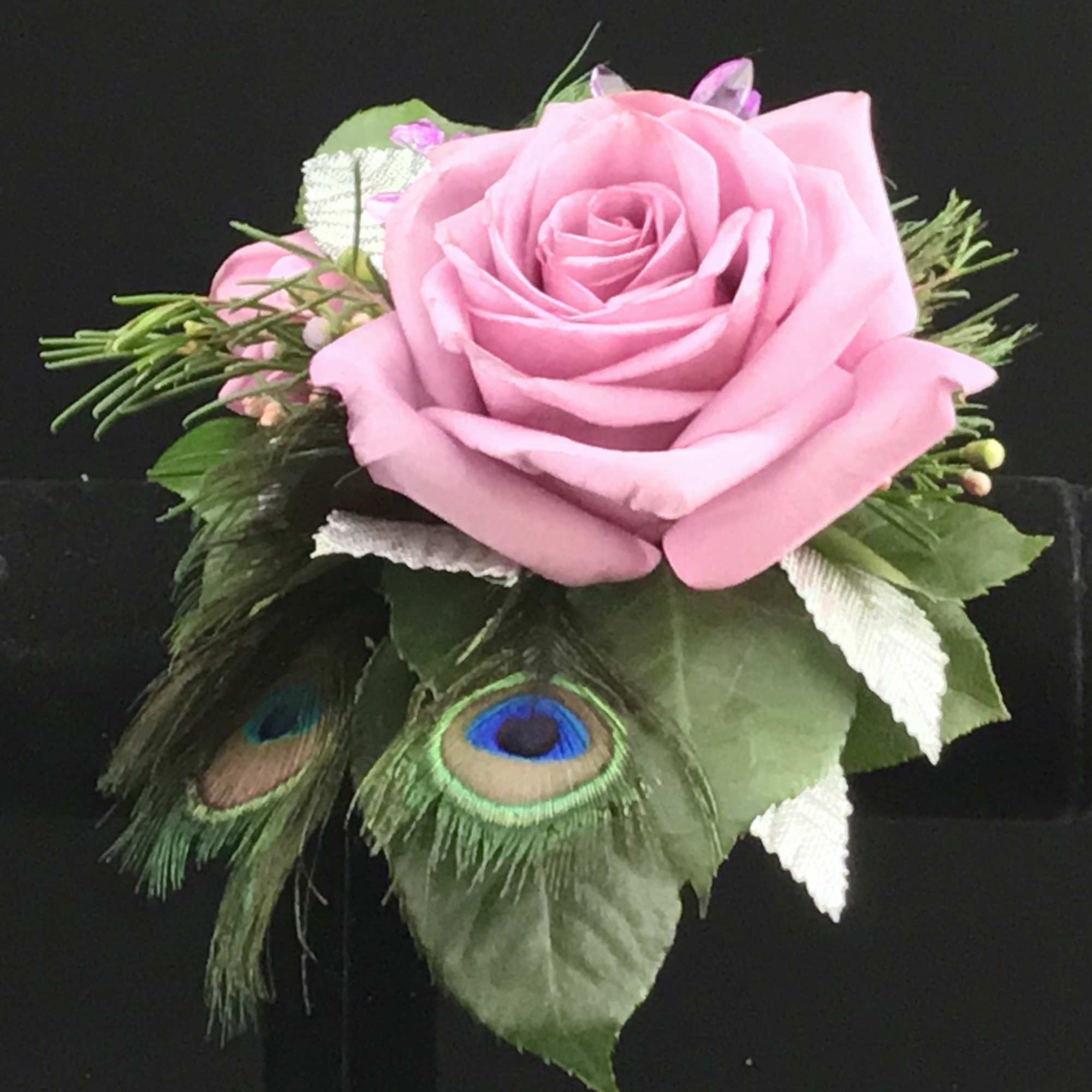 Pink rose boutonniere with peacock feathers and greenery