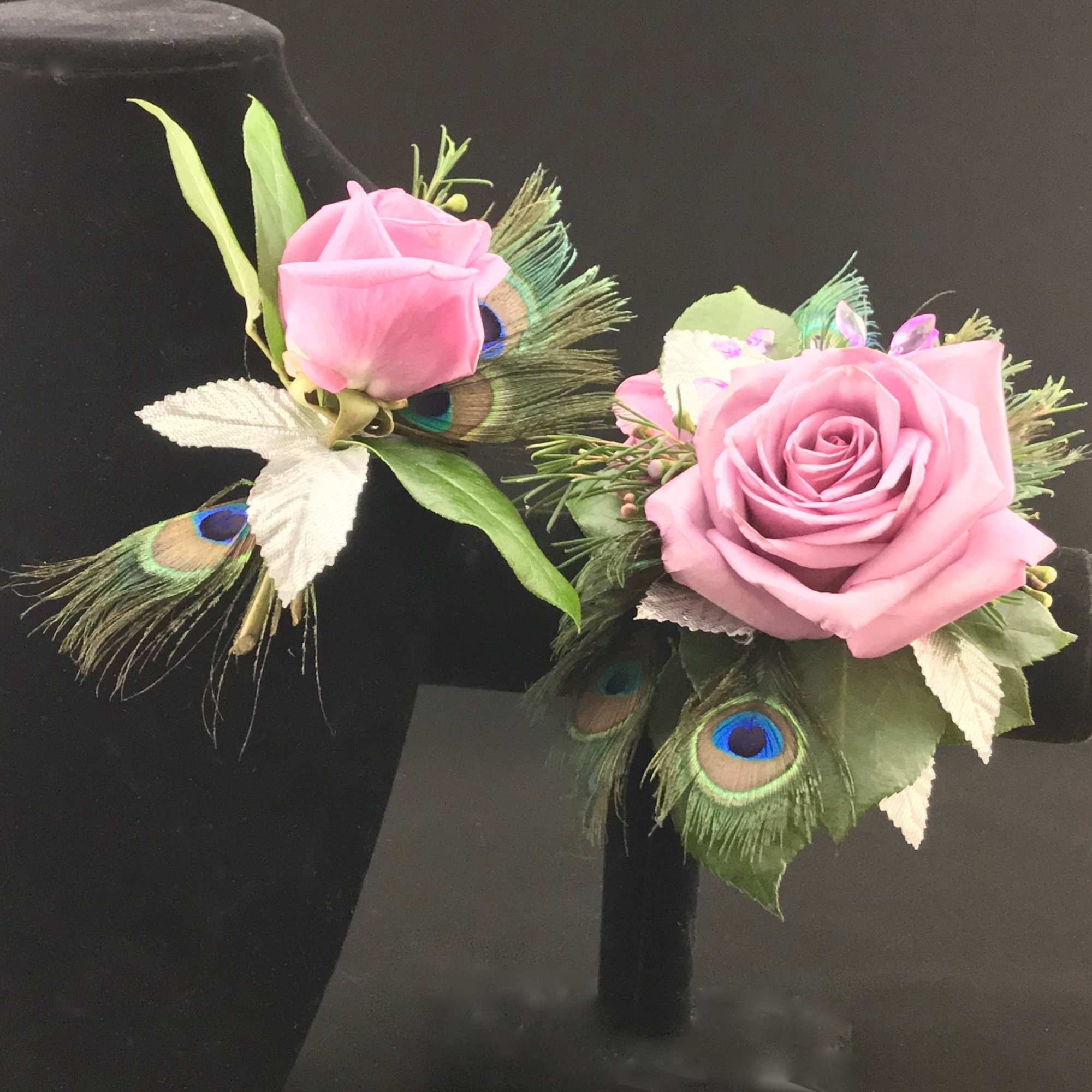 Pink rose boutonnieres with peacock feathers on black stands