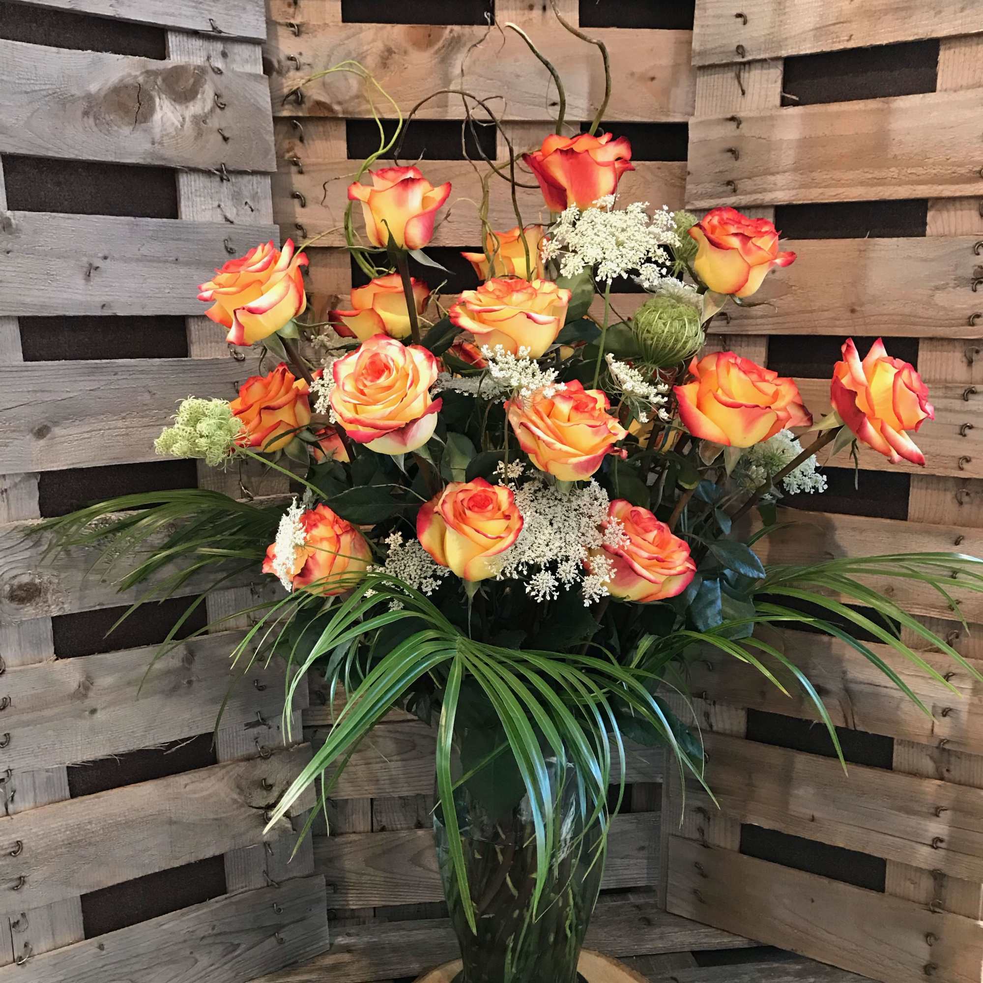 Orange and yellow roses in a tall glass vase with white filler flowers
