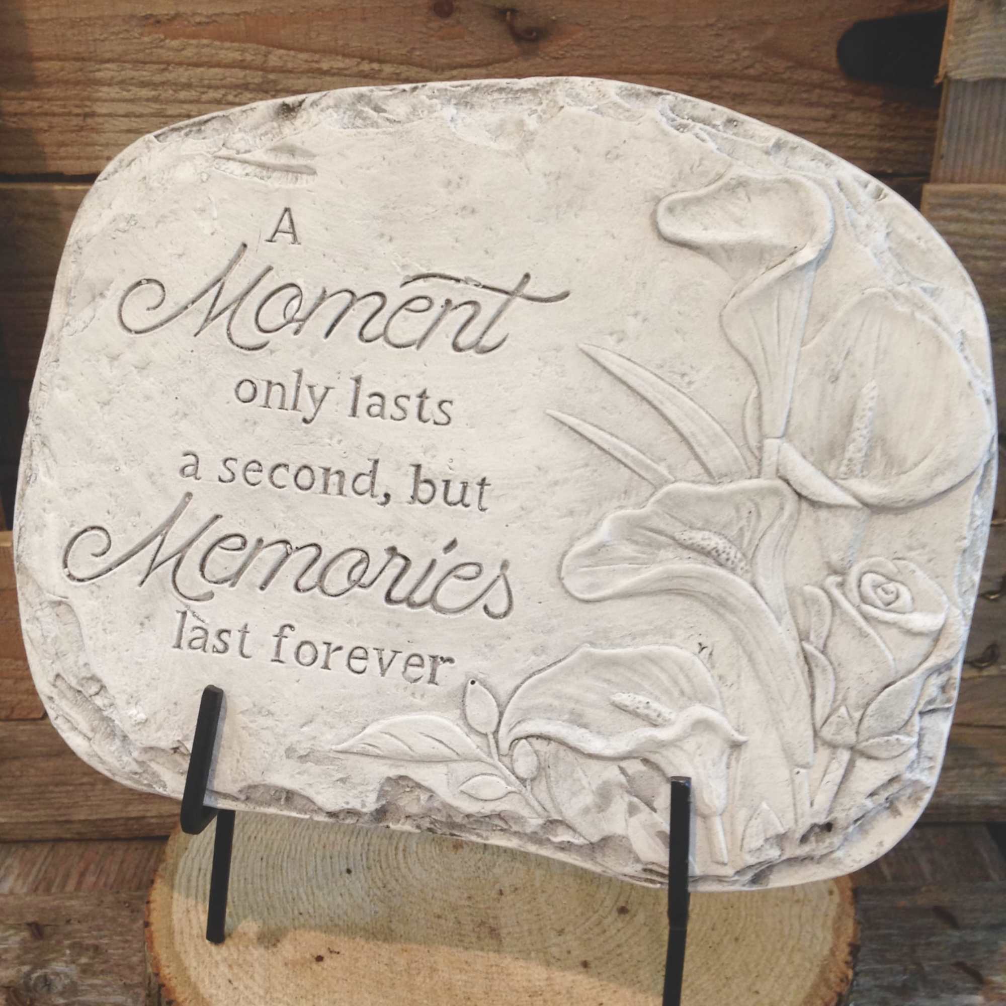 Engraved stone plaque with memorial quote and carved calla lilies and rose on a stand.