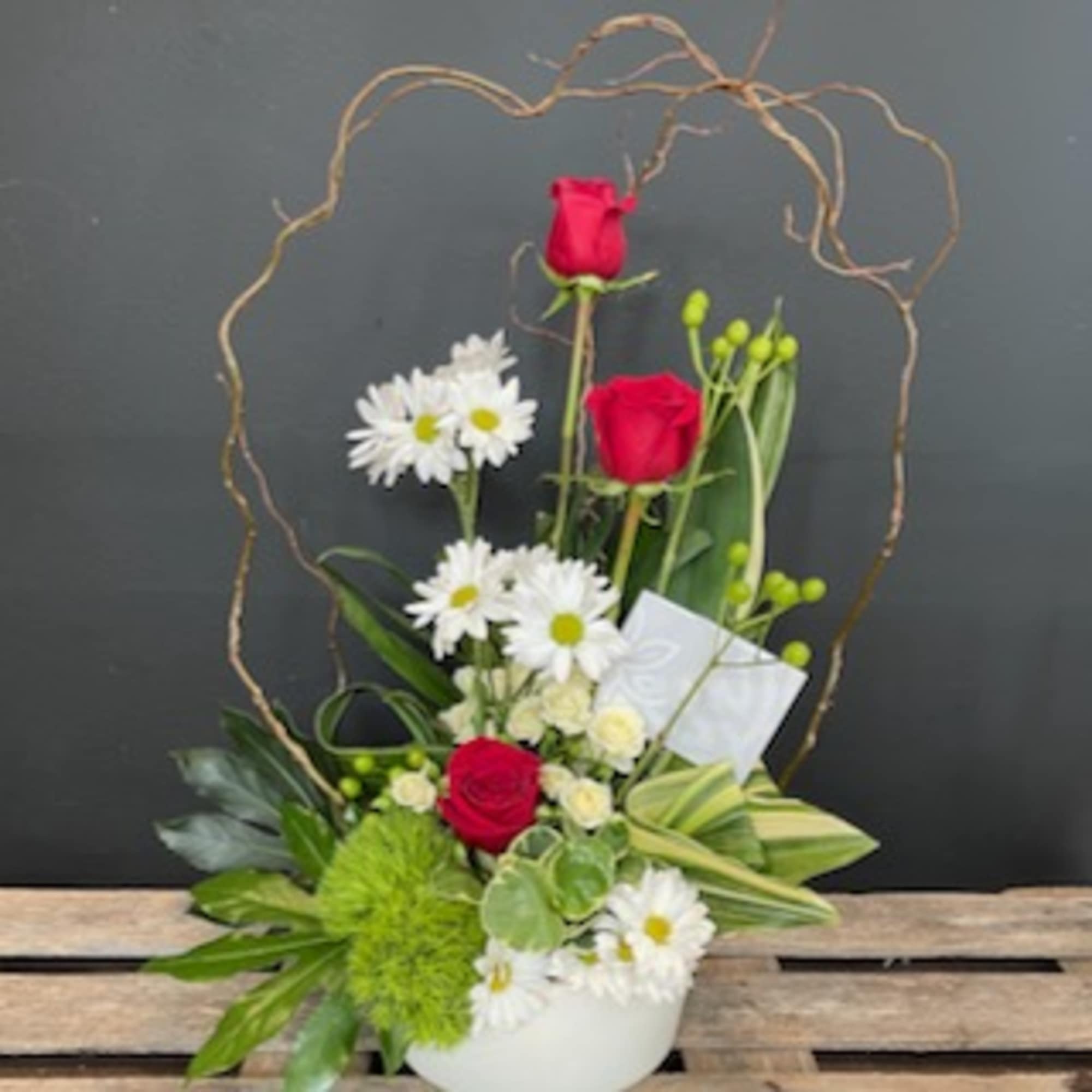 Red roses and white daisies in a white container with a twig heart frame