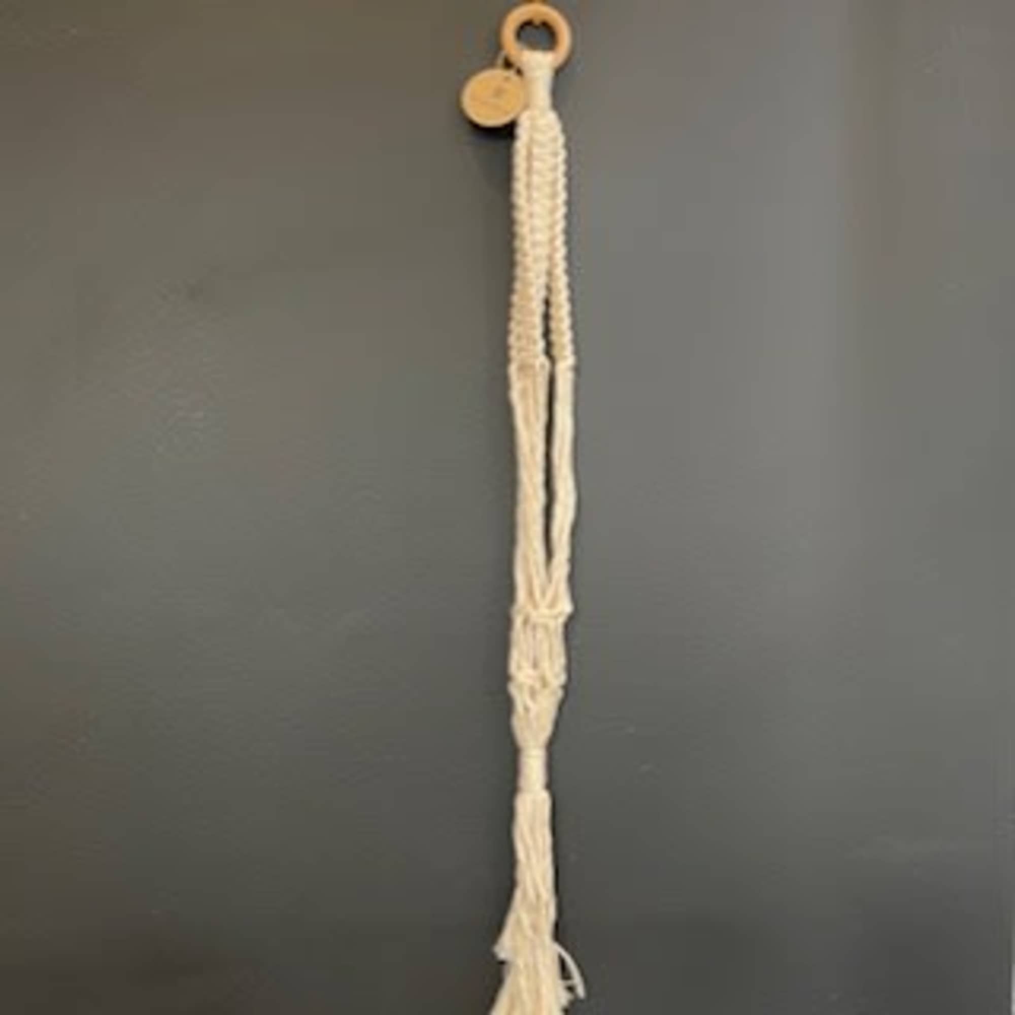 Macramé wall hanging with a wooden ring on a gray wall