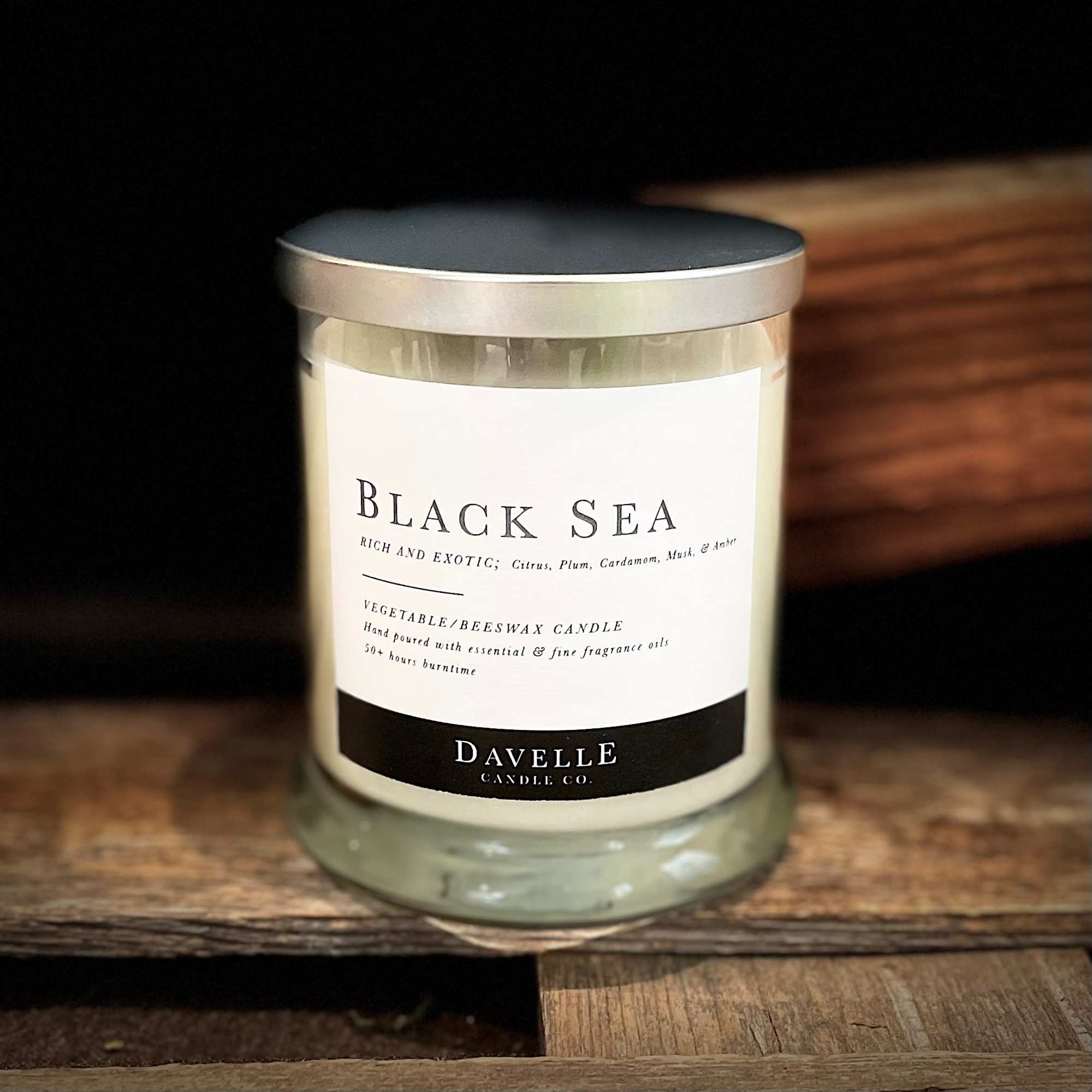 A labeled glass candle jar with a metal lid on a wooden surface