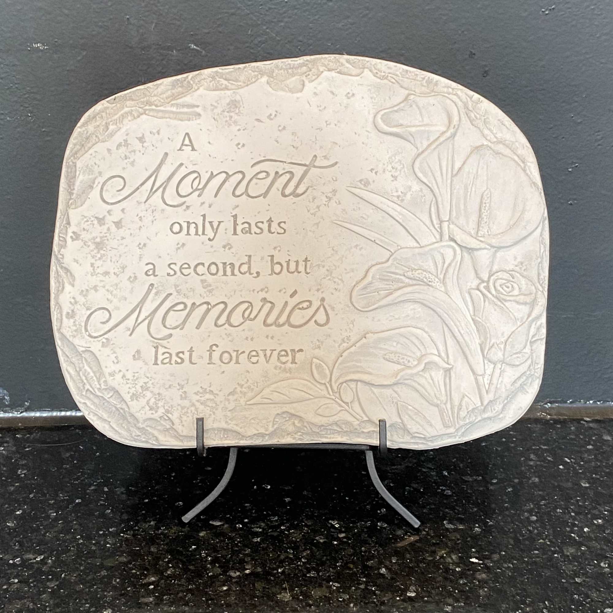 Beige stone memorial plaque with engraved quote and floral border on a black stand
