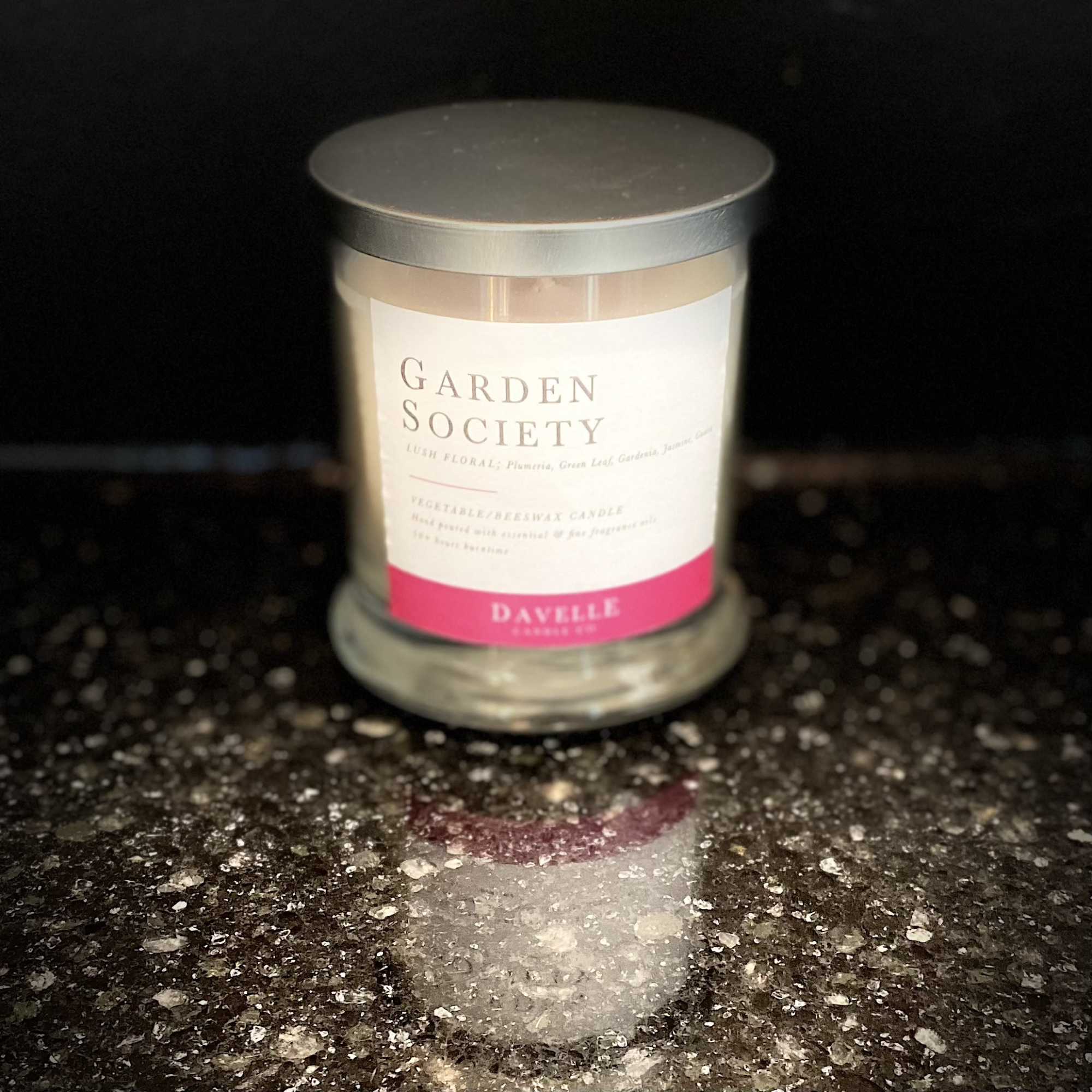 A glass candle jar with a silver lid and pink label