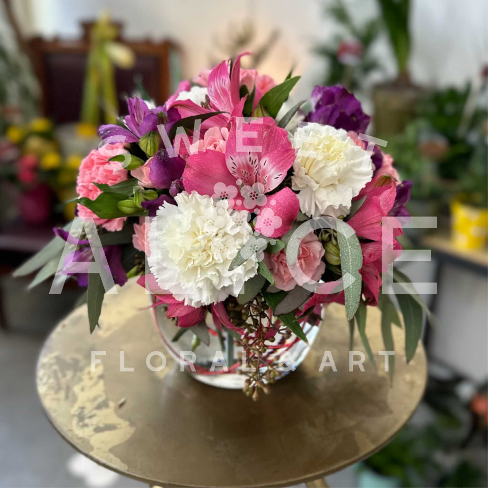 Compact arrangement of pink roses, white carnations, and purple alstroemeria in a clear glass vase