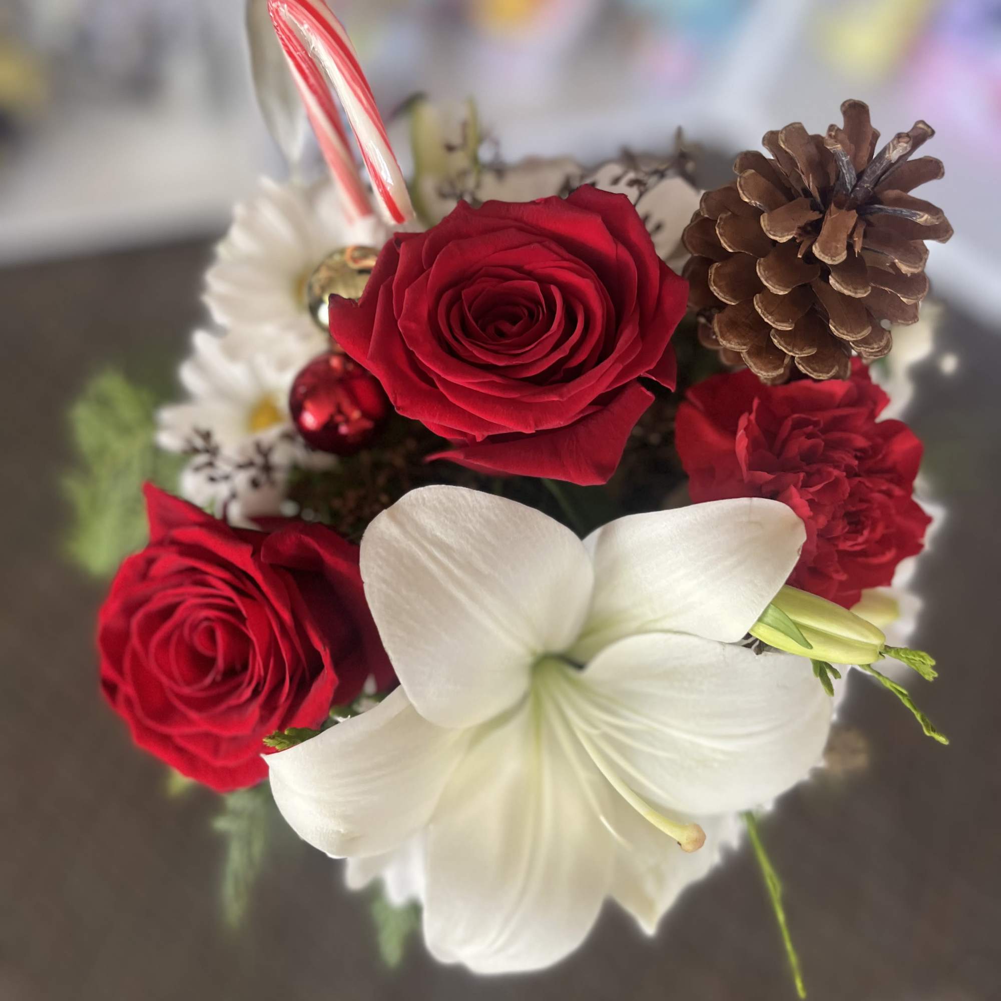 Red roses and a white lily with a candy cane and pinecone accents