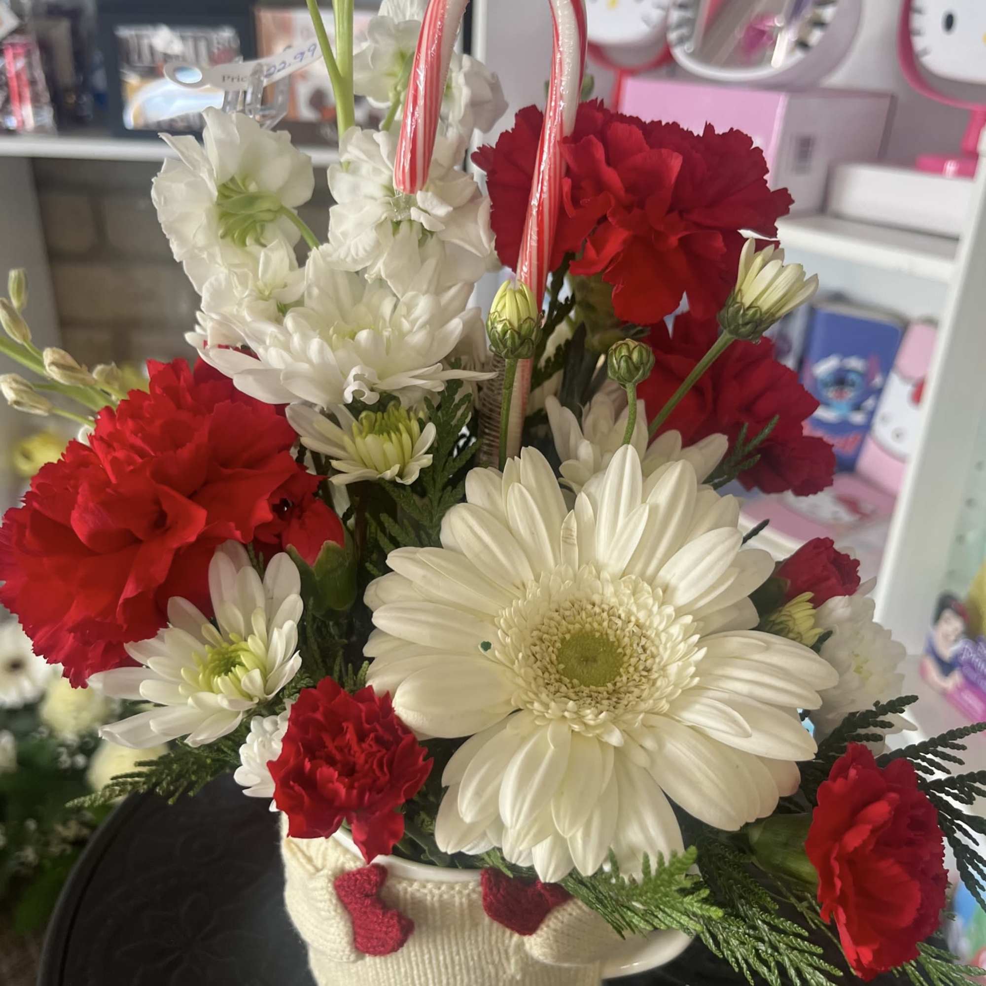 Red carnations and white daisies arranged in a small basket with candy canes.