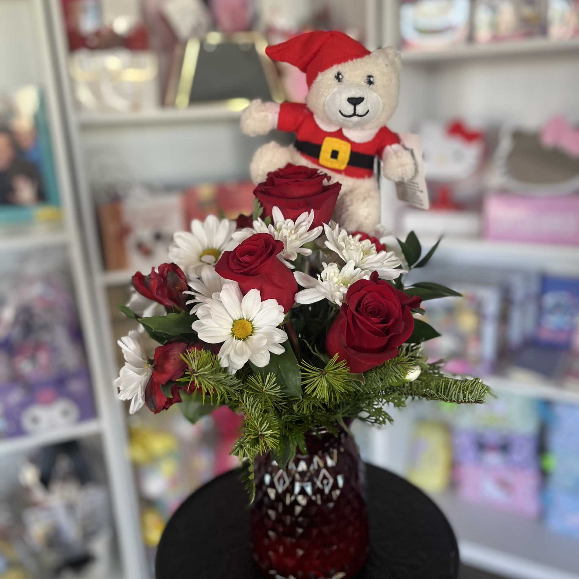 Red roses and white daisies in a red vase with a teddy bear in a Santa outfit