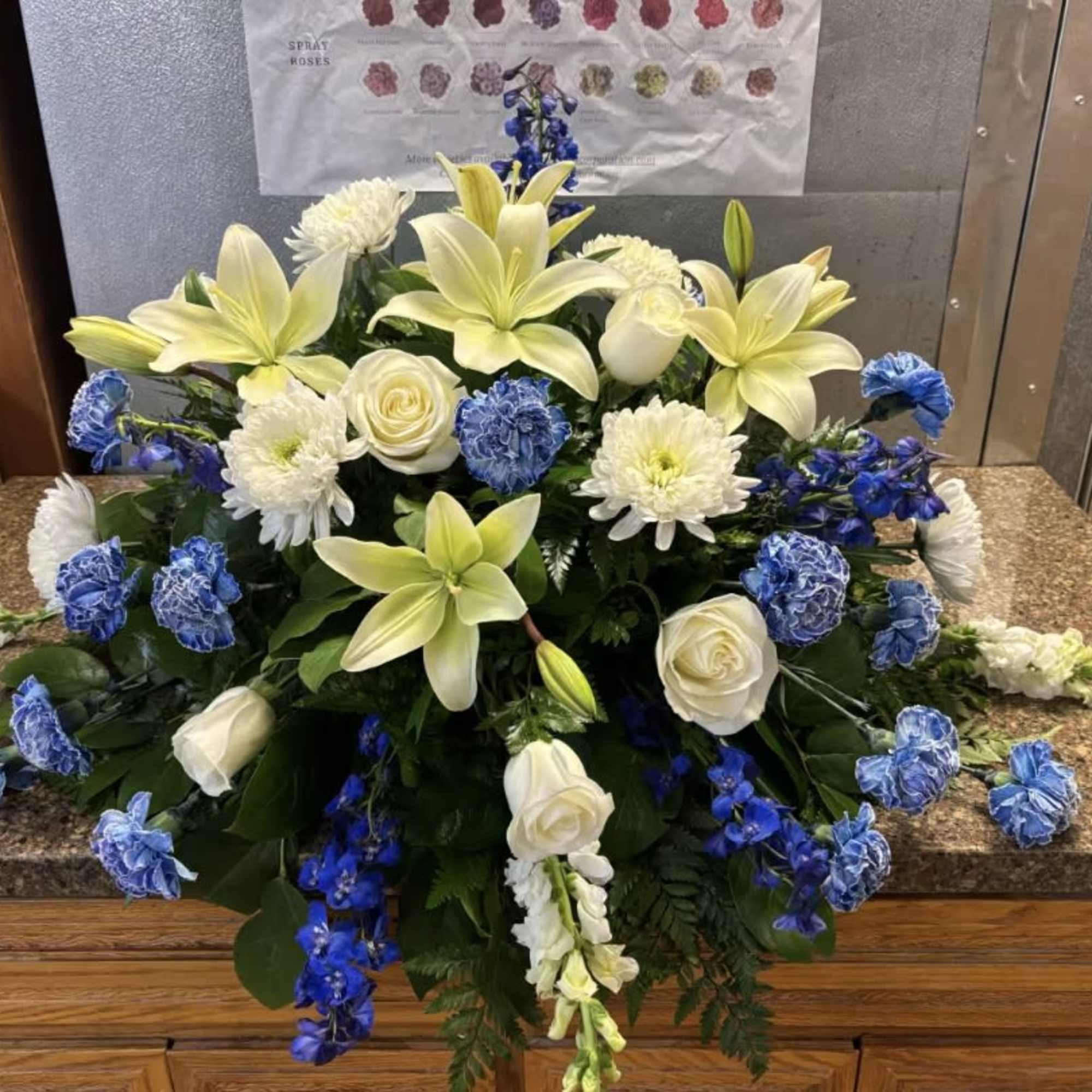 White lilies, roses, and blue flowers arranged in a casket spray