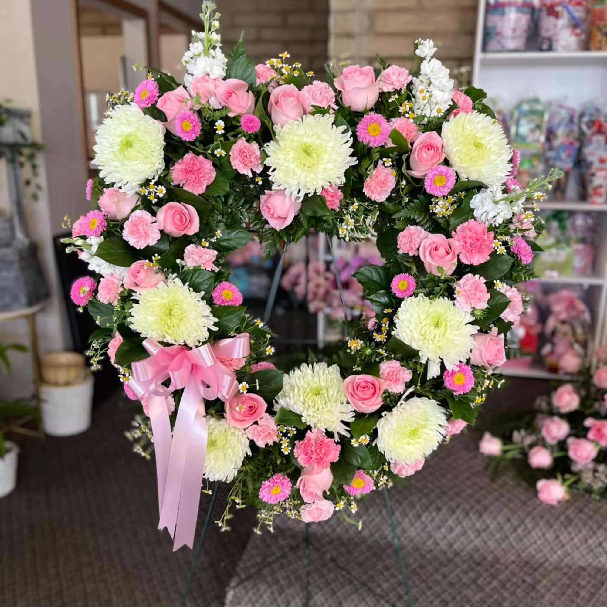 Heart-shaped floral wreath with pink roses and white mums on an easel