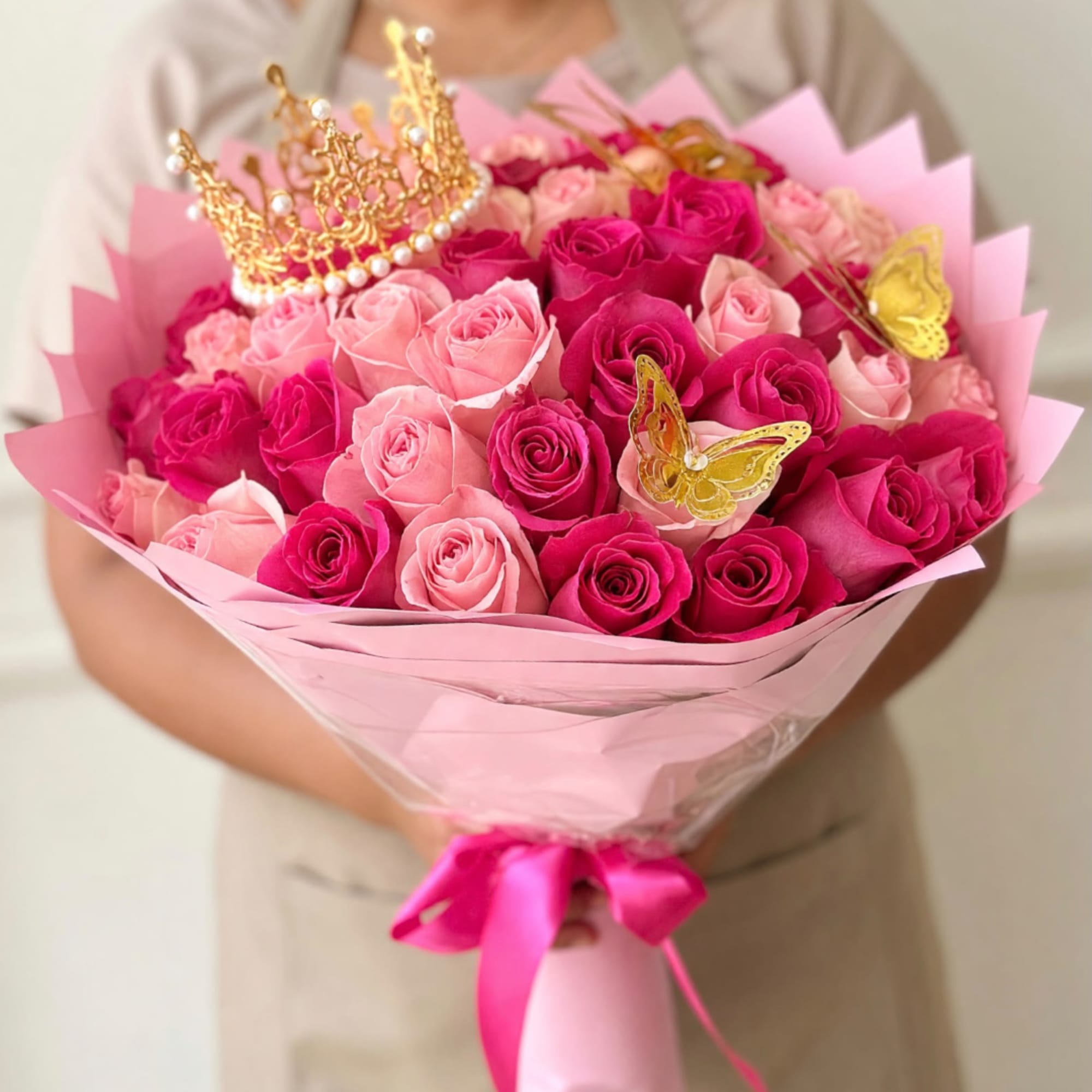 Pink and magenta rose bouquet wrapped in pink paper with gold crown and butterfly picks