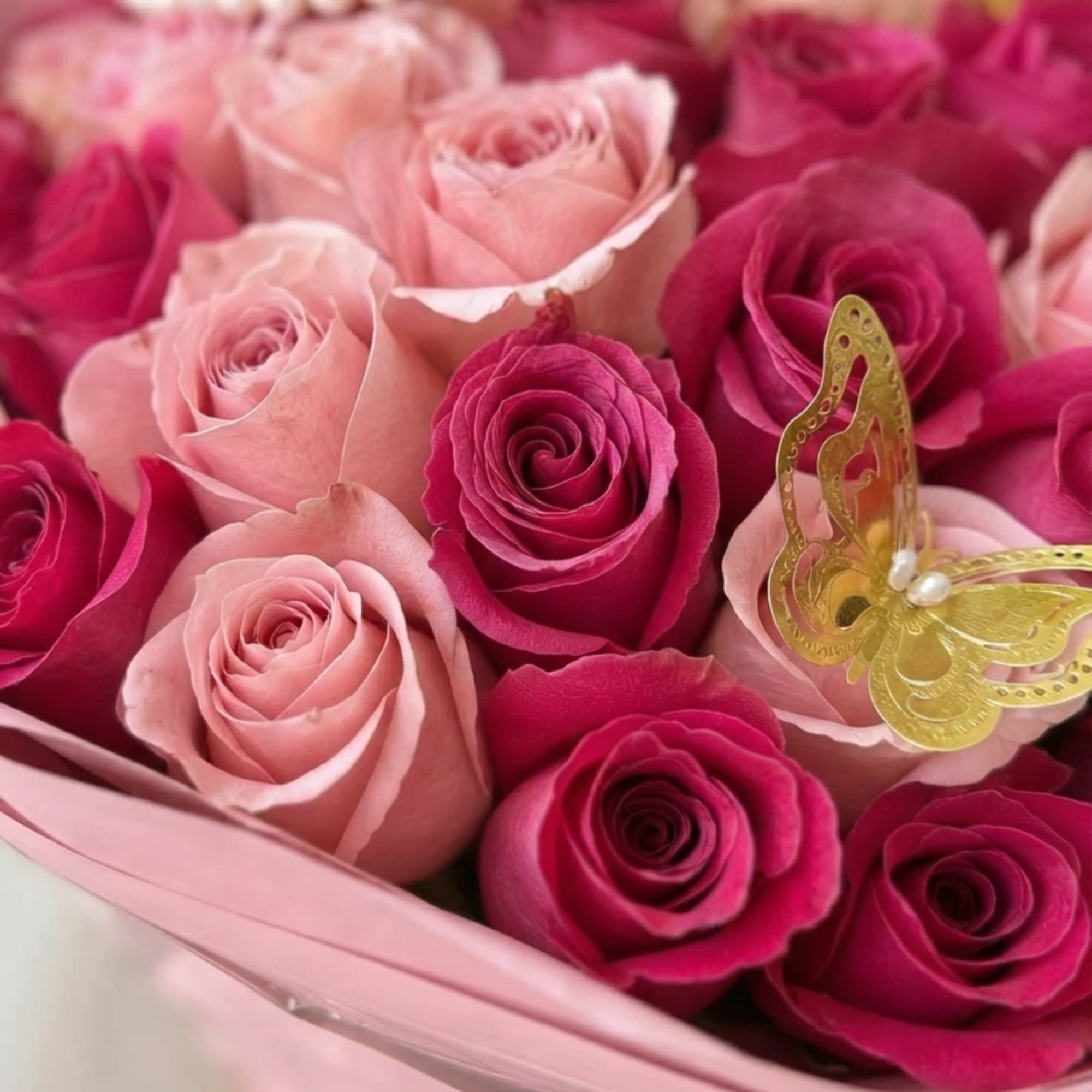 Pink and magenta roses arranged in a bouquet with a gold butterfly decoration