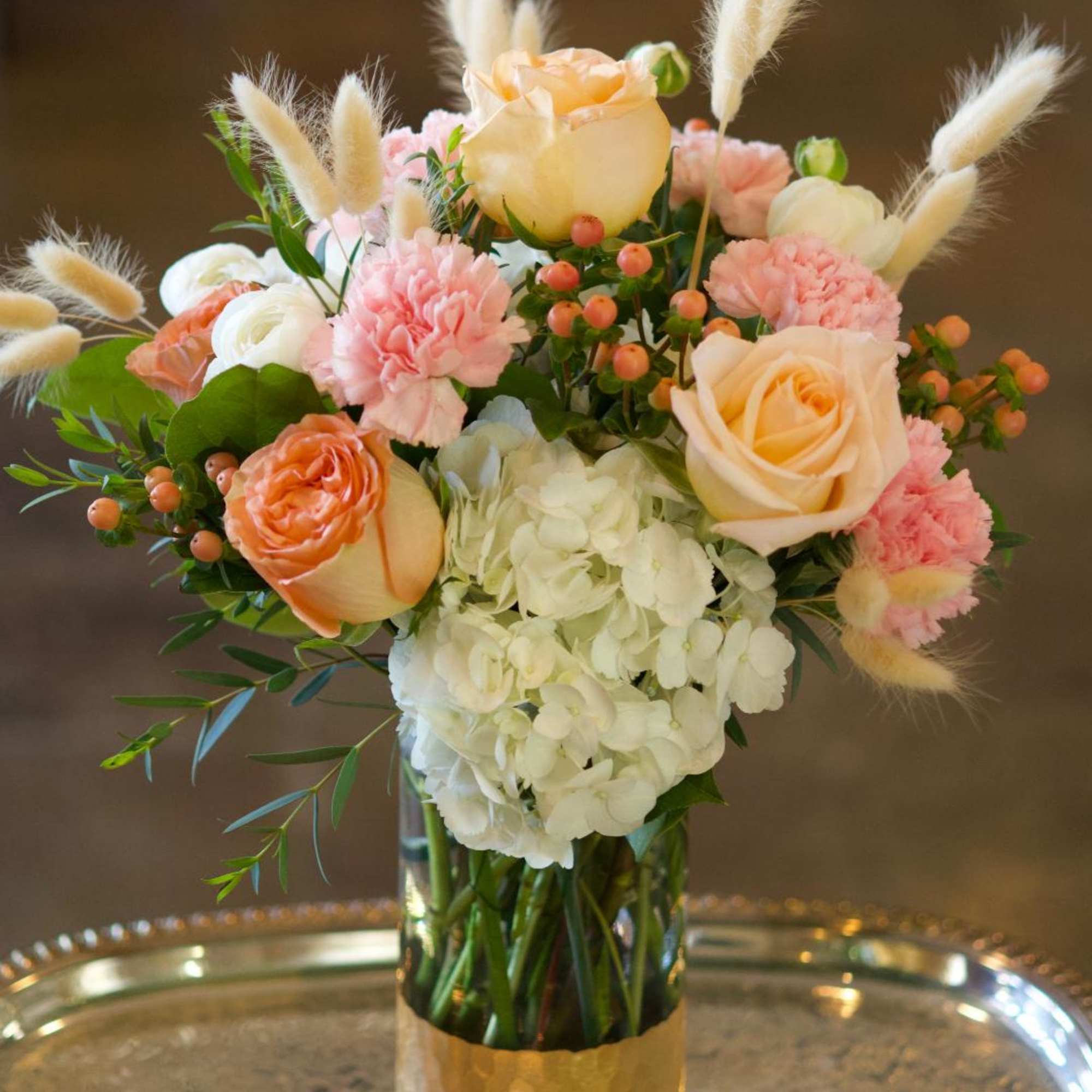 Peach and white bouquet in a glass vase with fluffy accents