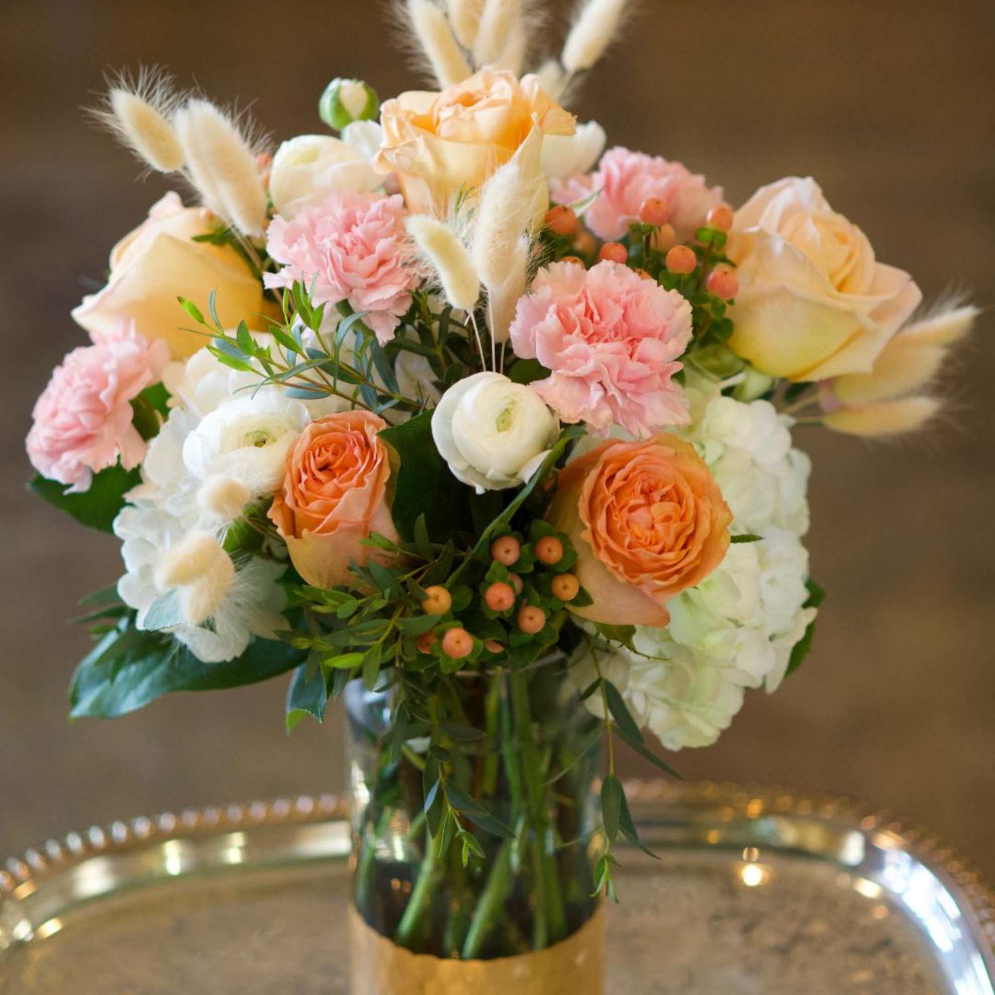 Peach and pink bouquet in a glass vase with fluffy white accents