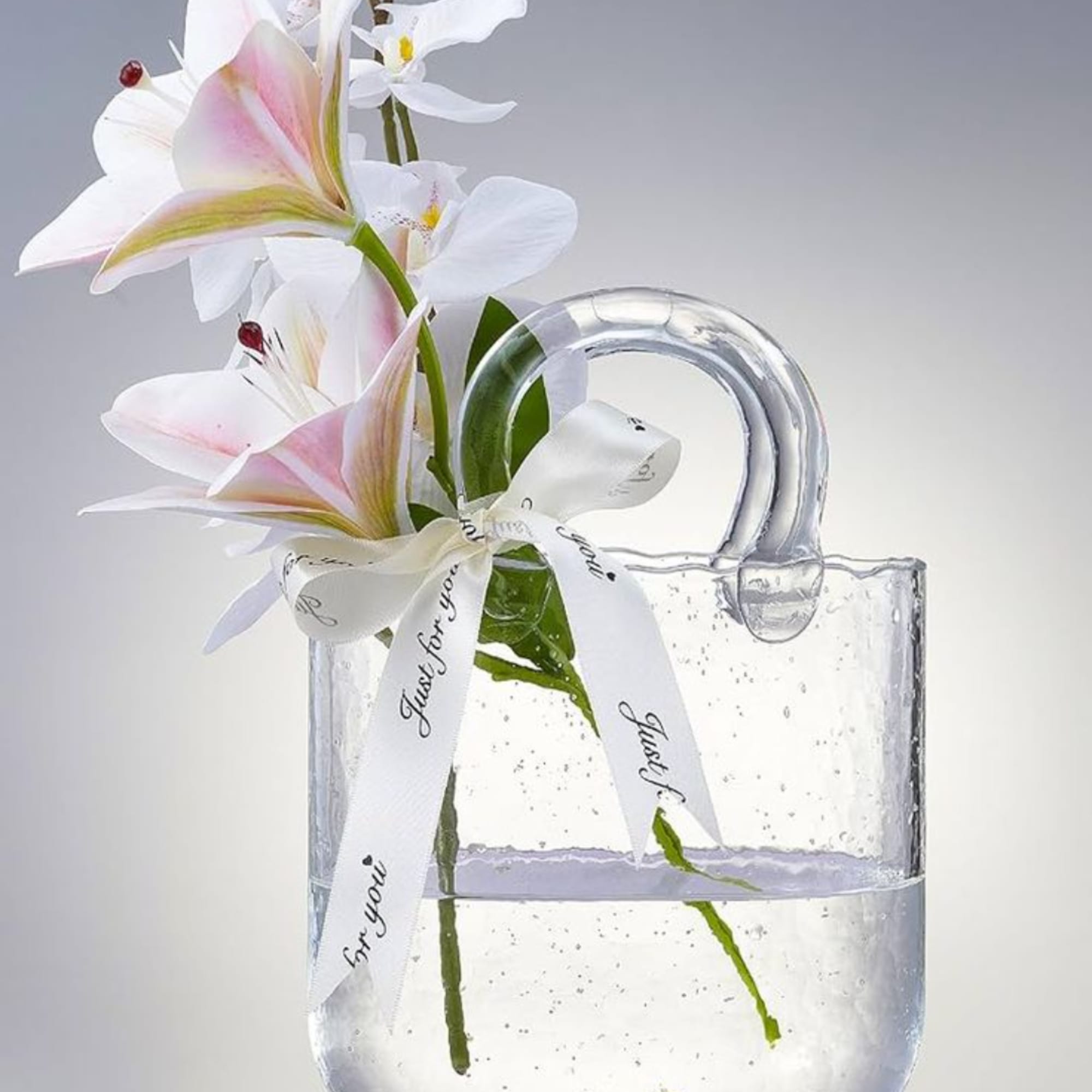 White lilies in a clear glass mug with a ribbon bow
