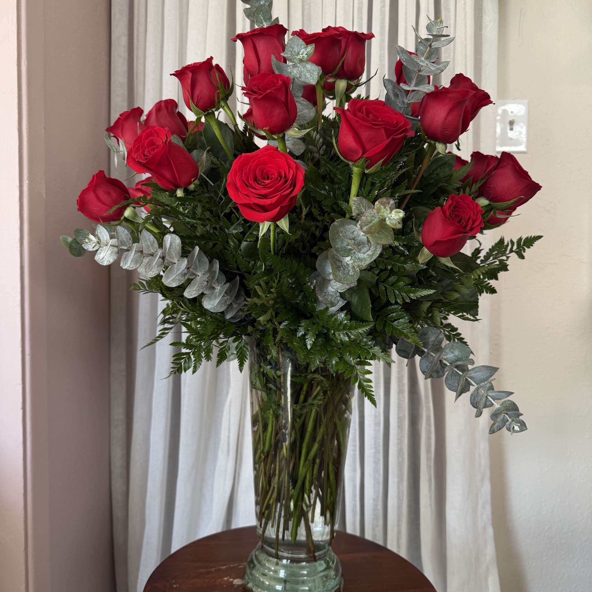 Red roses in a clear glass vase with silver eucalyptus