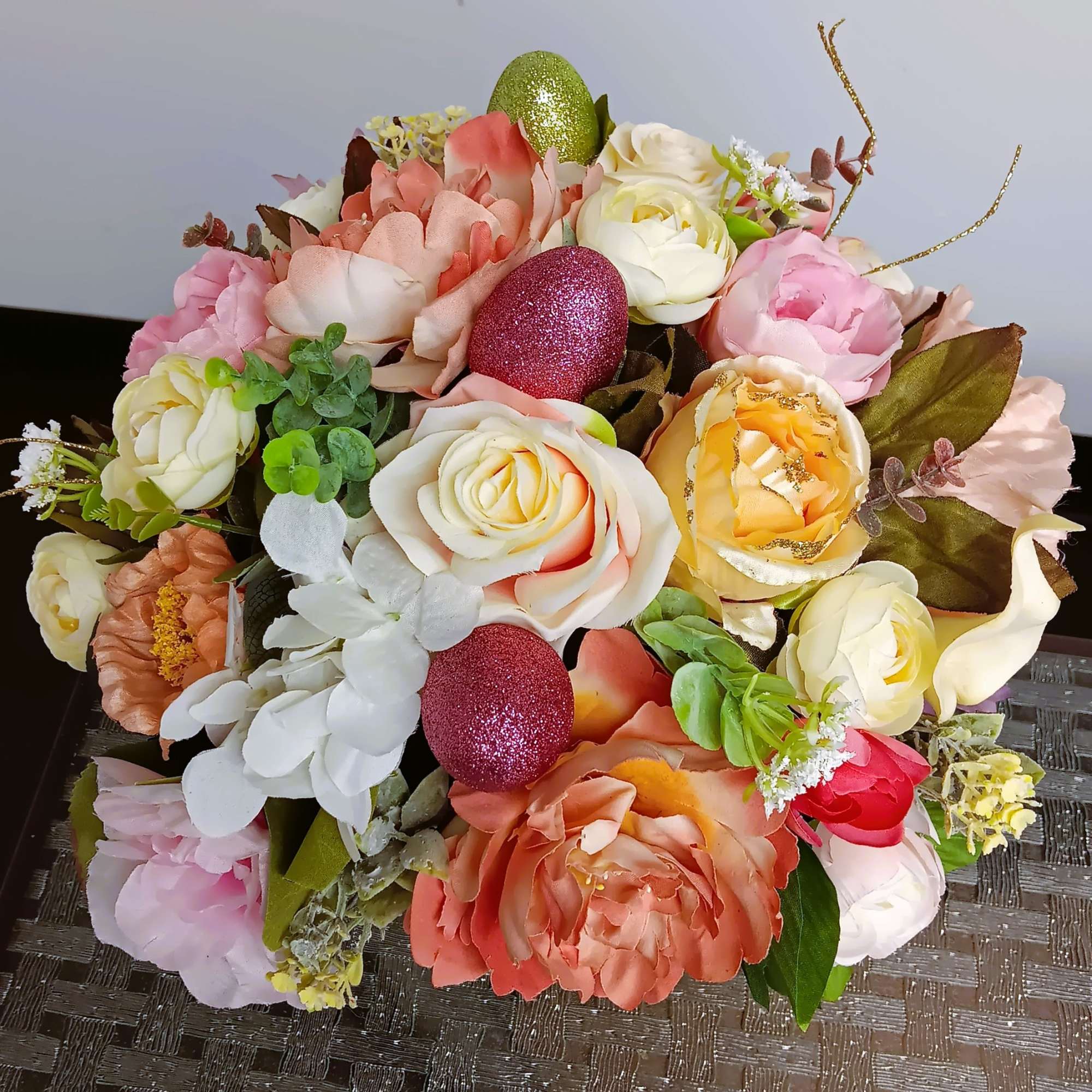 Round bouquet of pastel roses and peonies with glittery decorative eggs in spring colors