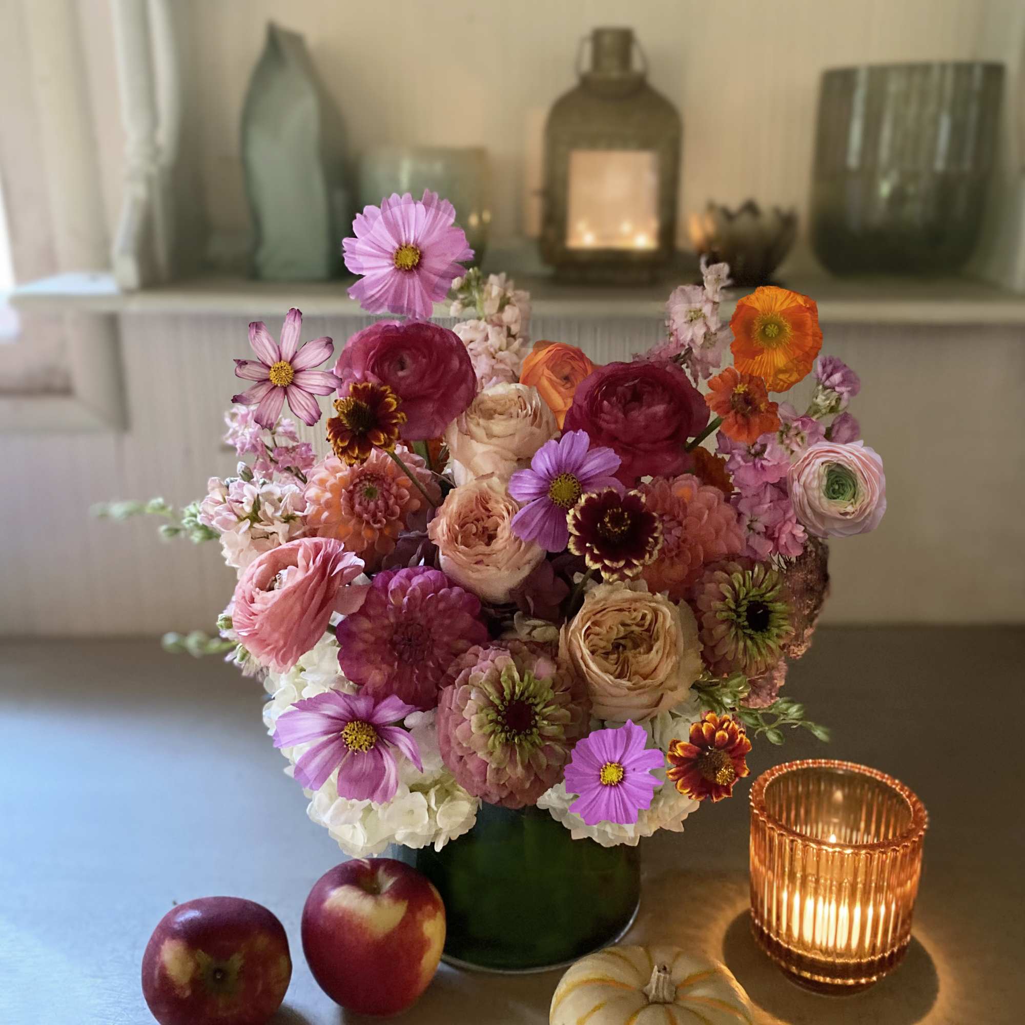 Mixed pink and orange flower arrangement in a green vase with candles and small pumpkins