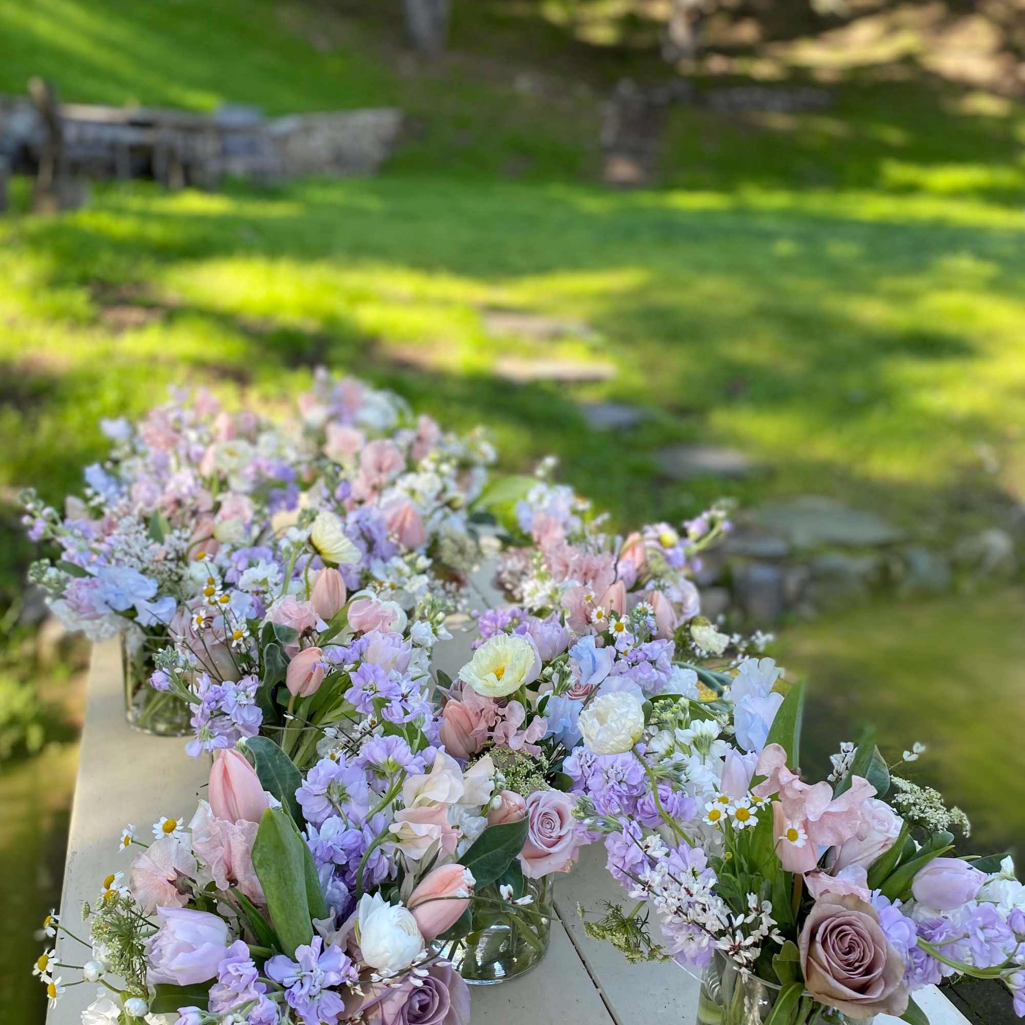 Pastel floral centerpieces in glass vases on a table outdoors