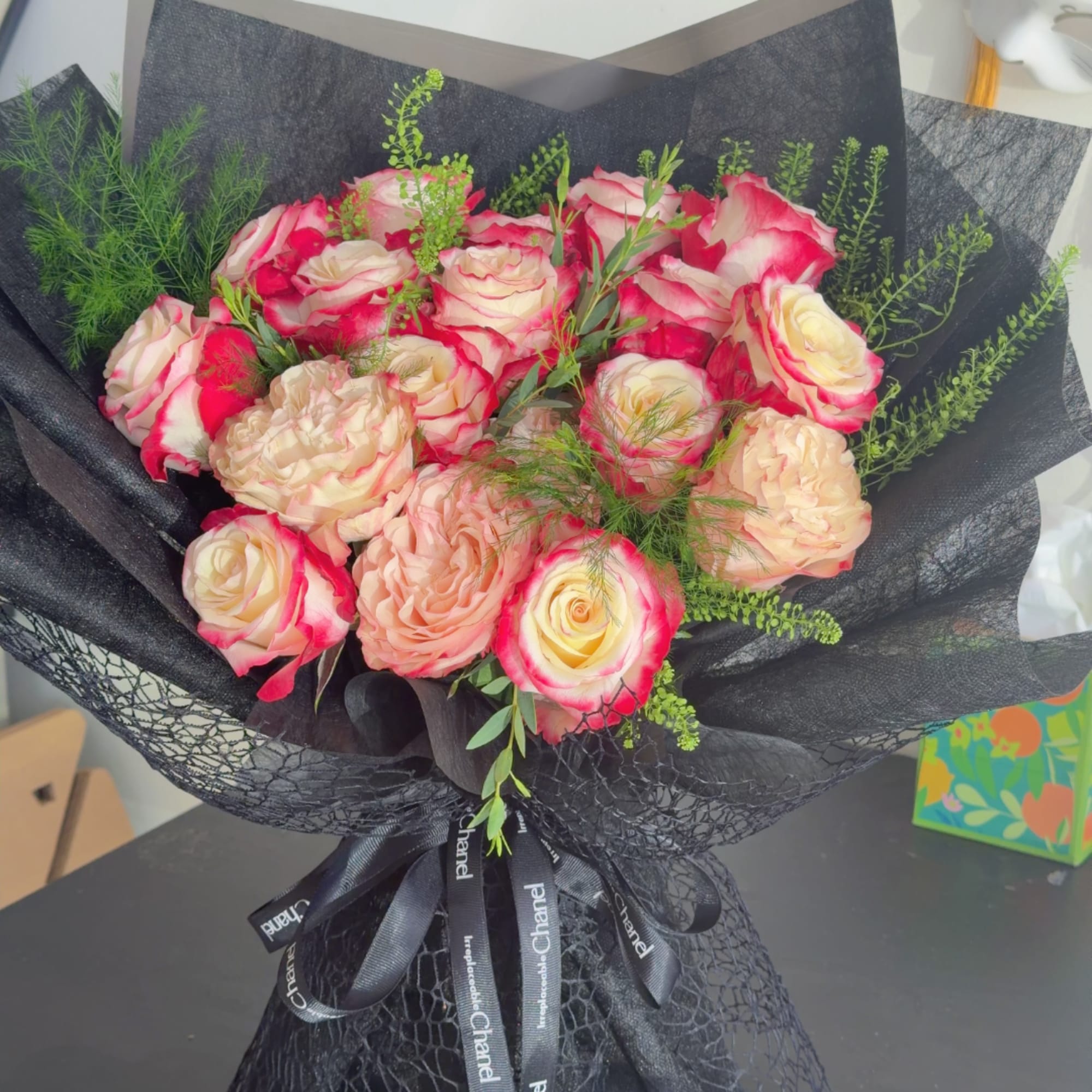Pink and cream roses in black wrapping with a ribbon bow