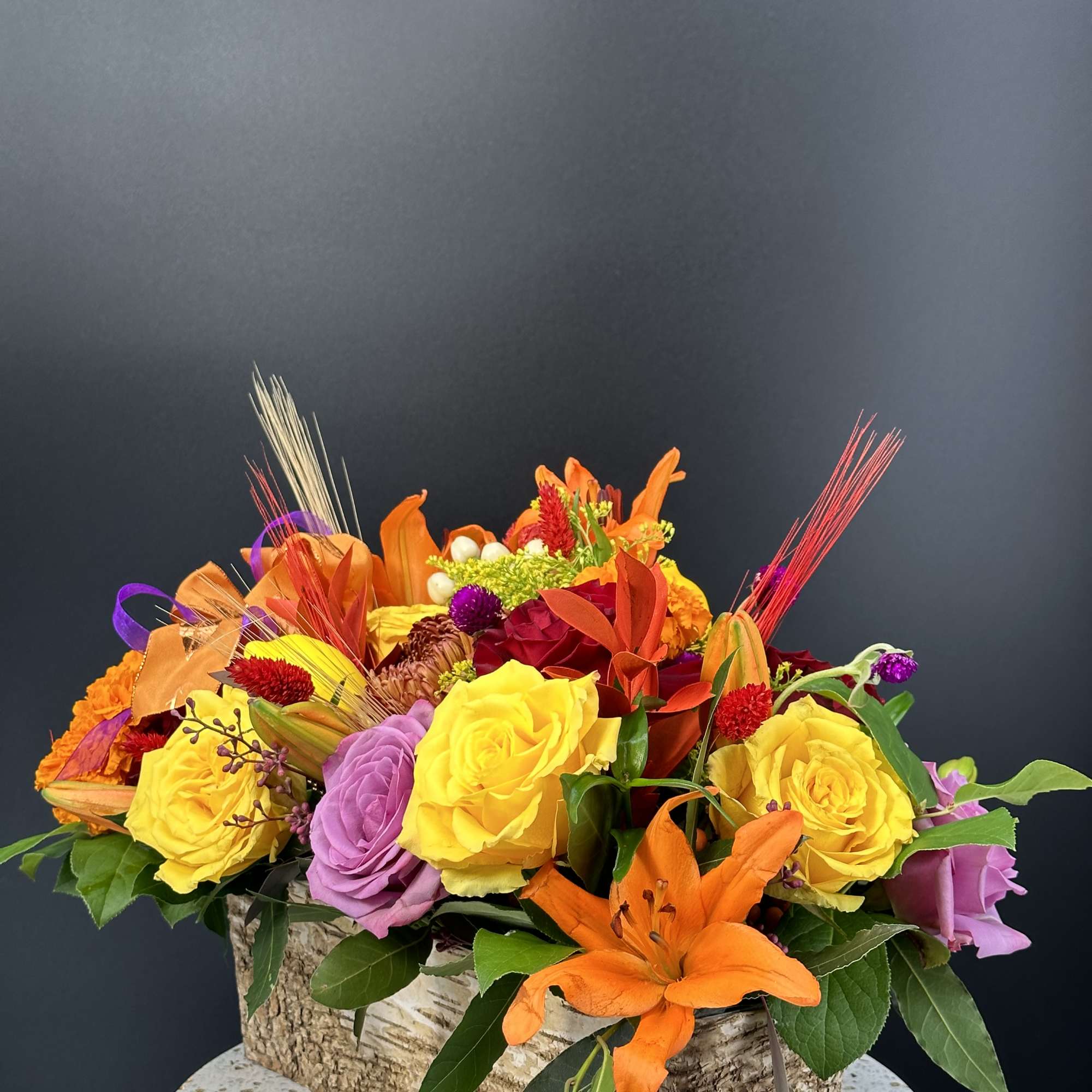 Bright mixed bouquet with roses and lilies in a bark-covered container