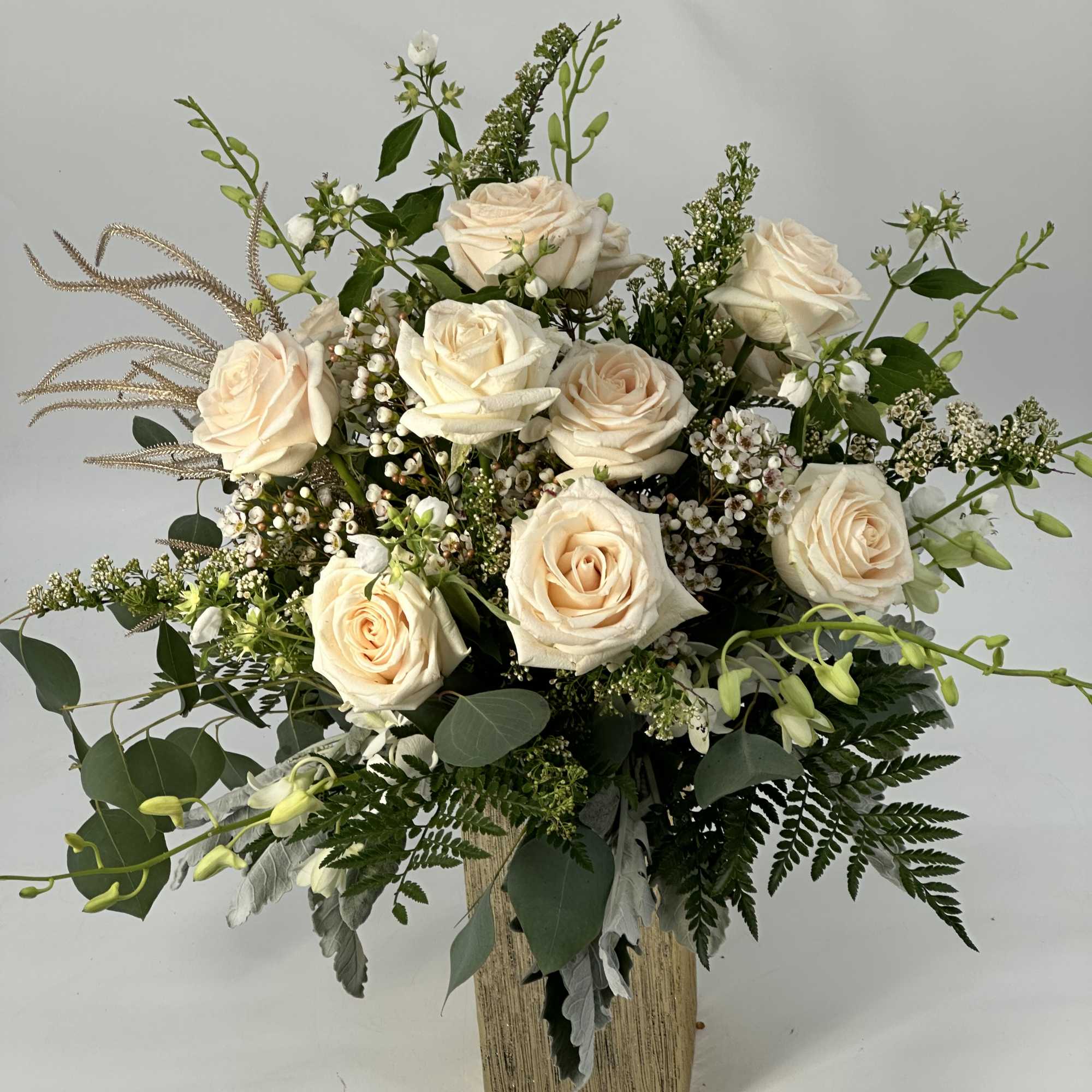 Cream roses in a tall rectangular vase with mixed greenery