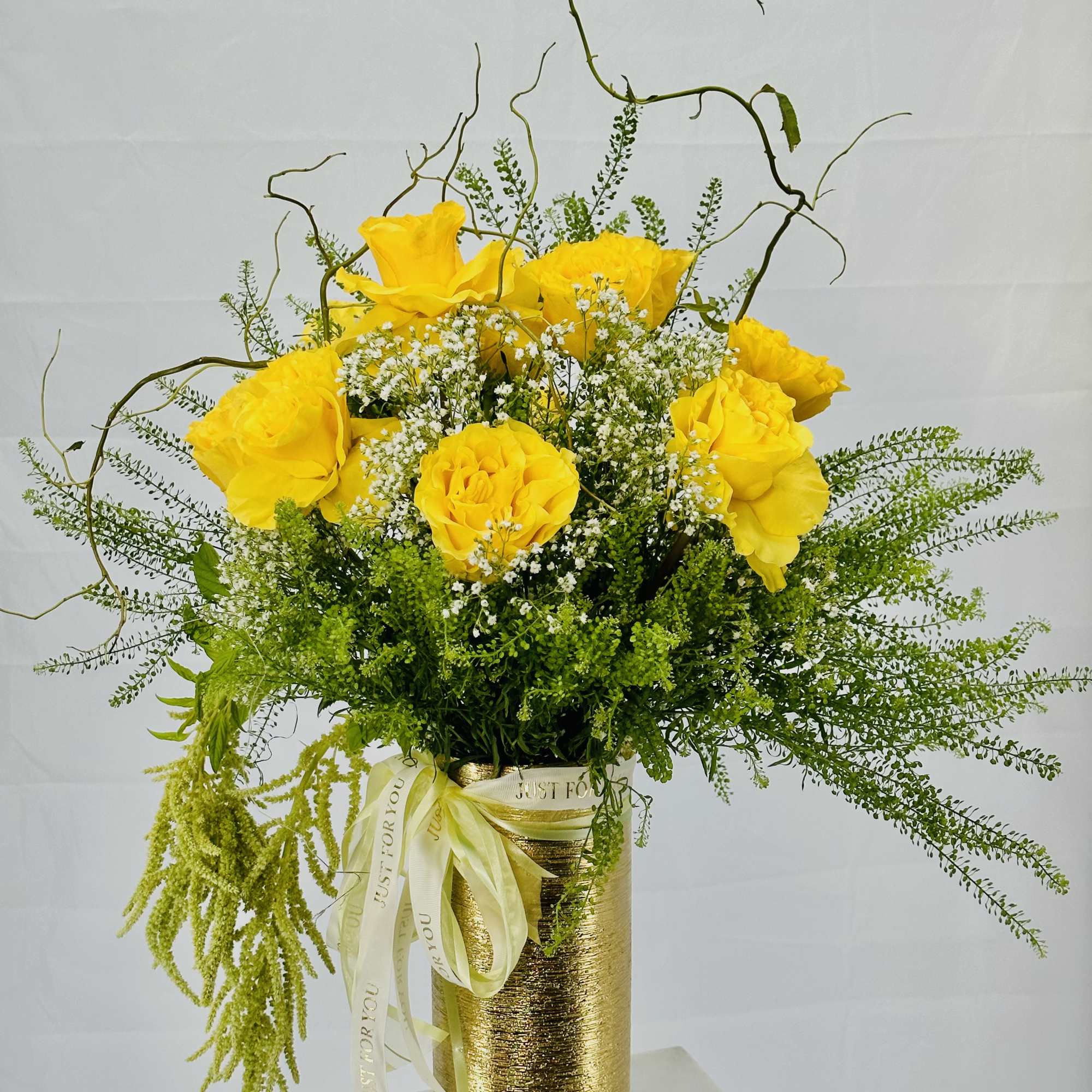 Yellow roses in a gold vase with airy white filler flowers