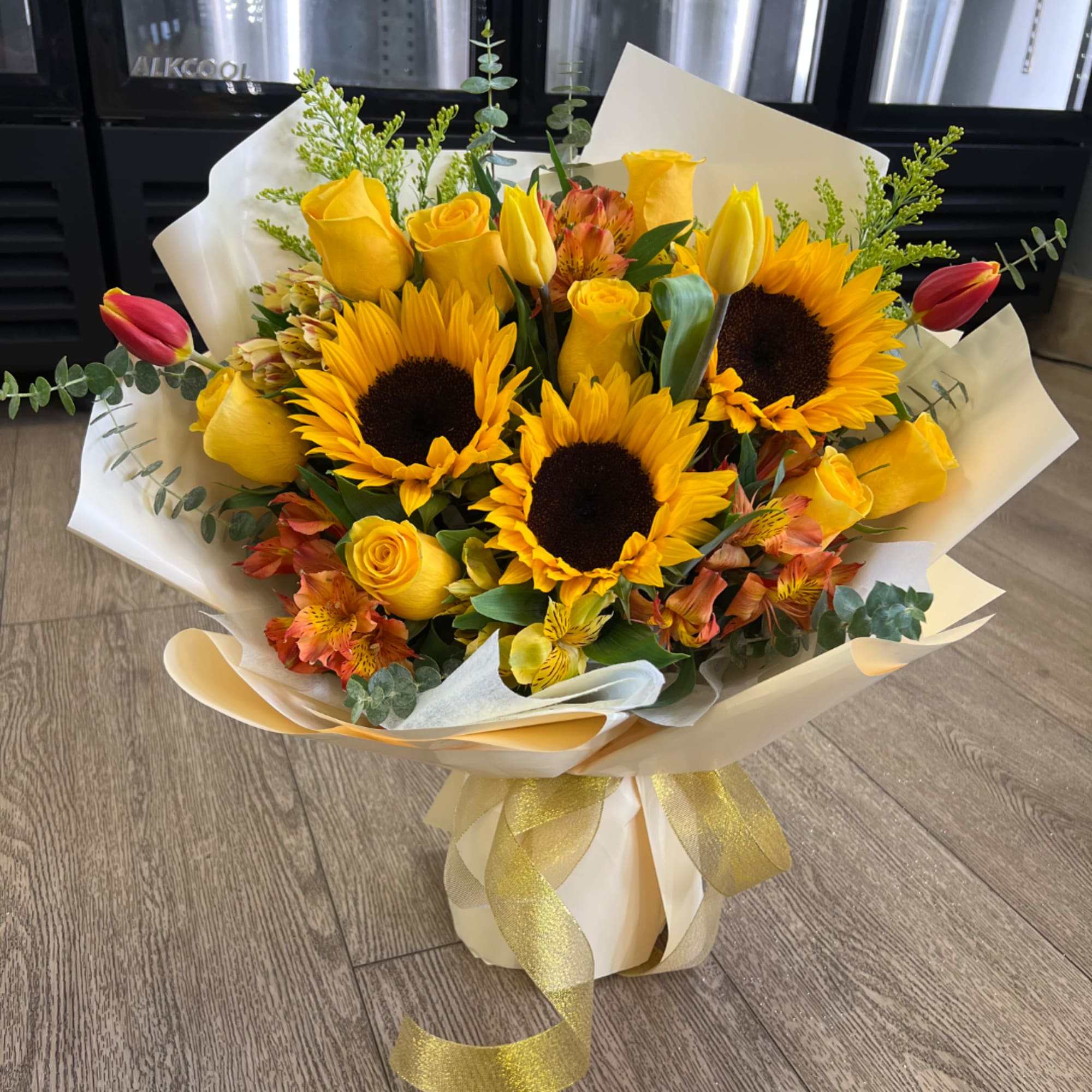 Bouquet of sunflowers, yellow roses, and tulips wrapped in white paper