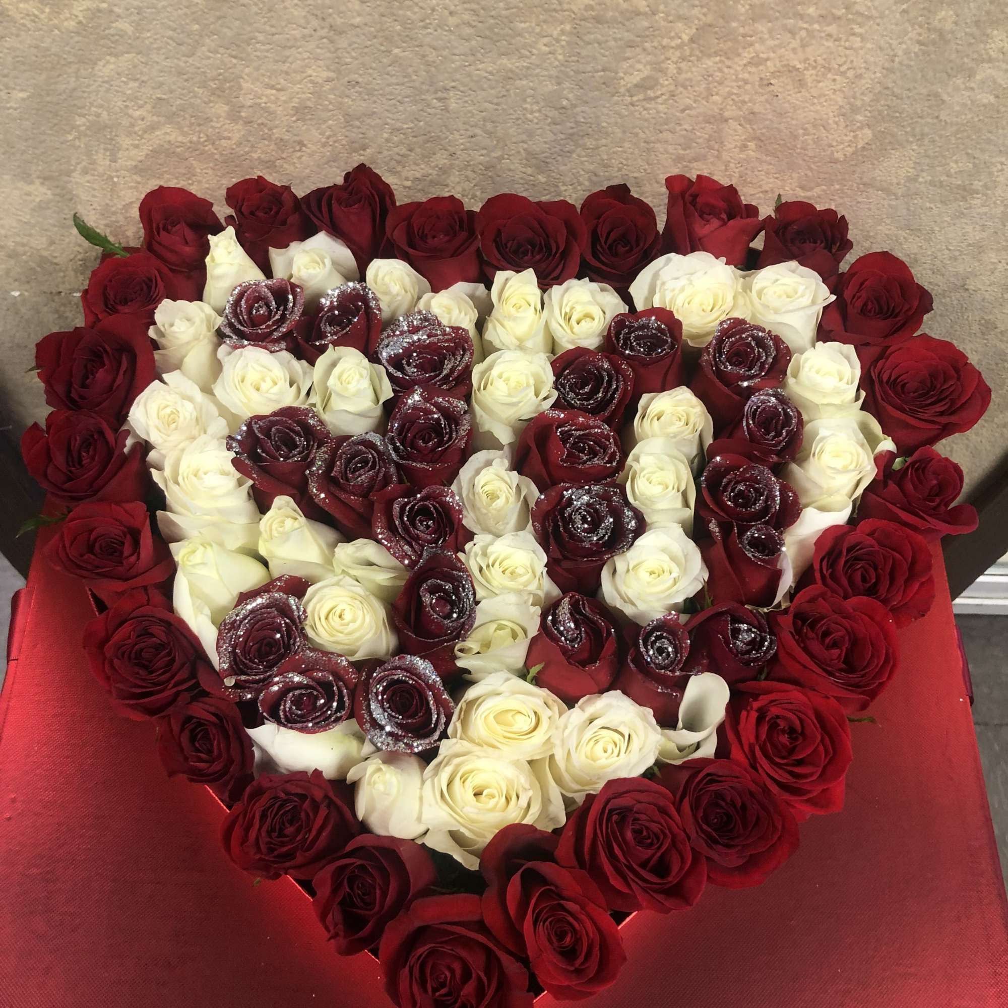 Heart-shaped arrangement of red and white roses in a red box