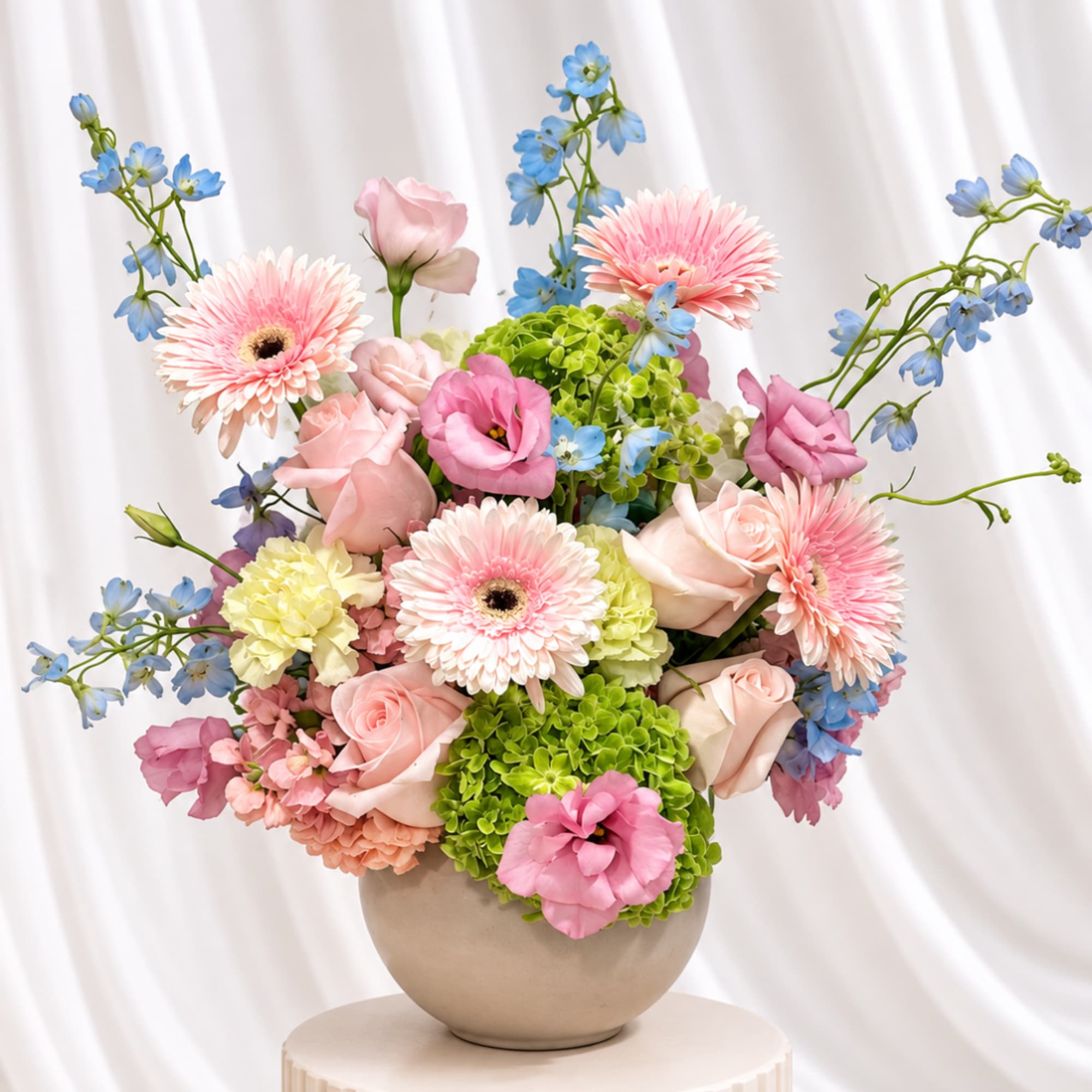 Pastel bouquet of pink roses, gerbera daisies, and blue flowers in a round vase