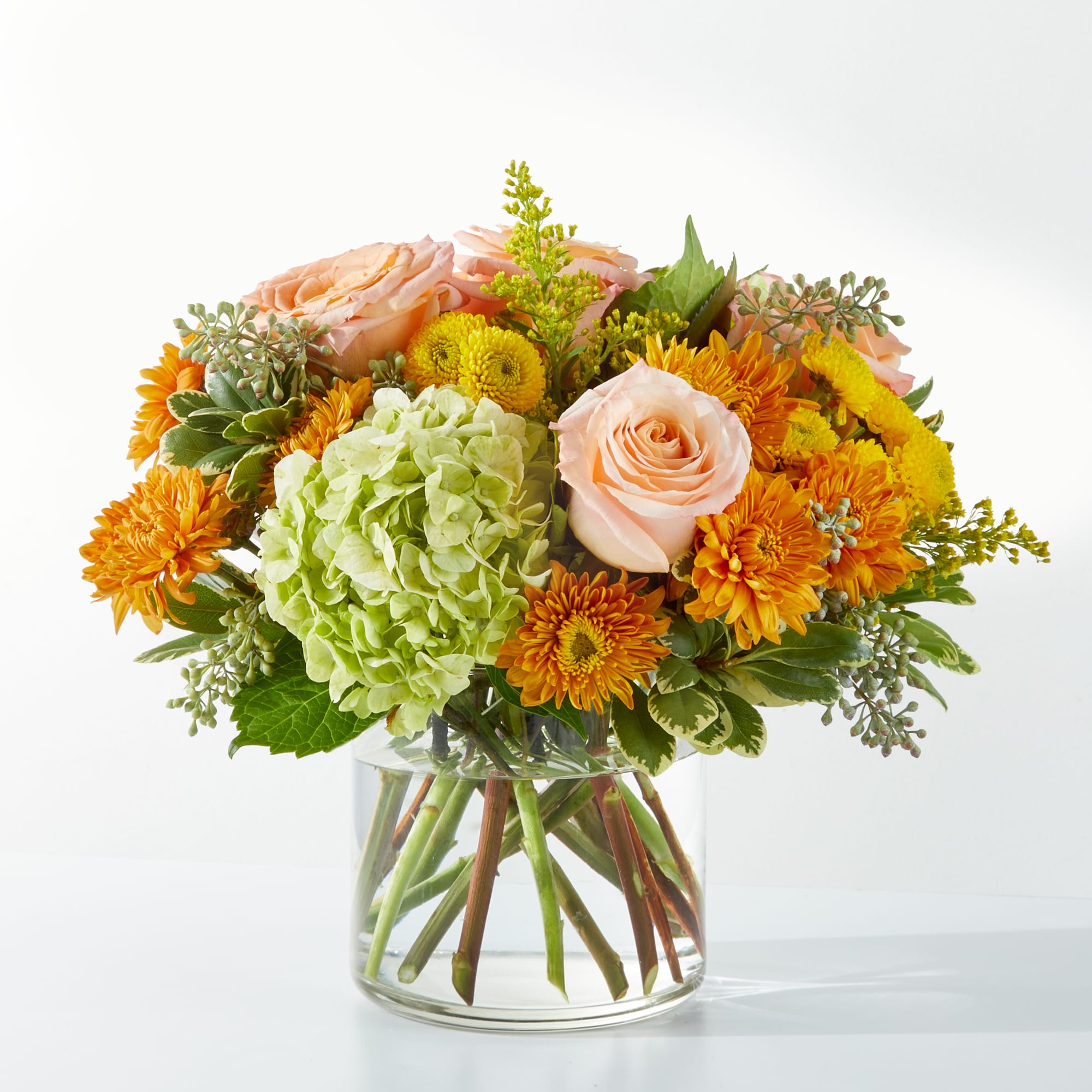 Peach roses and orange mums in a clear glass vase with a green hydrangea bloom