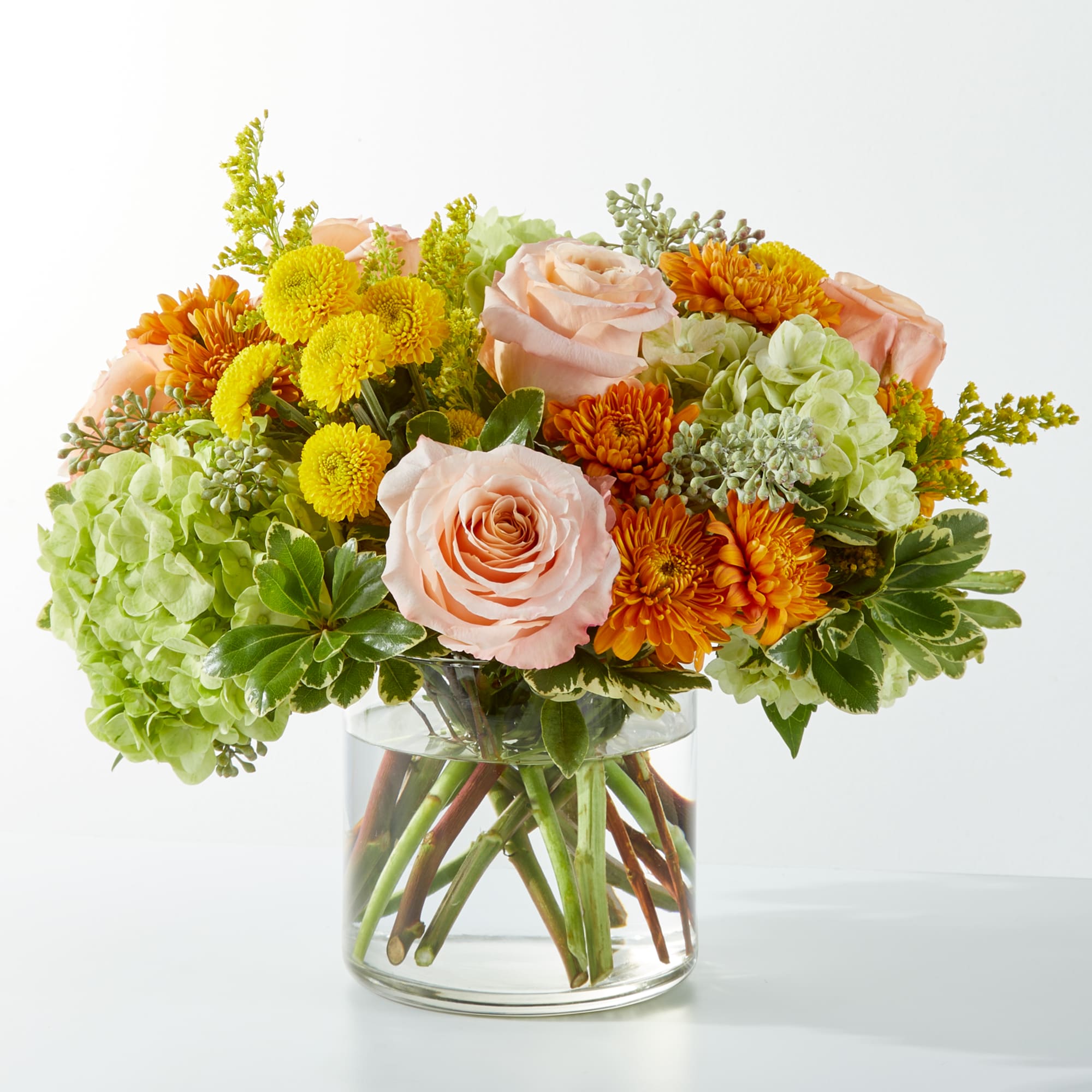 Peach roses and orange-yellow mums in a clear glass vase
