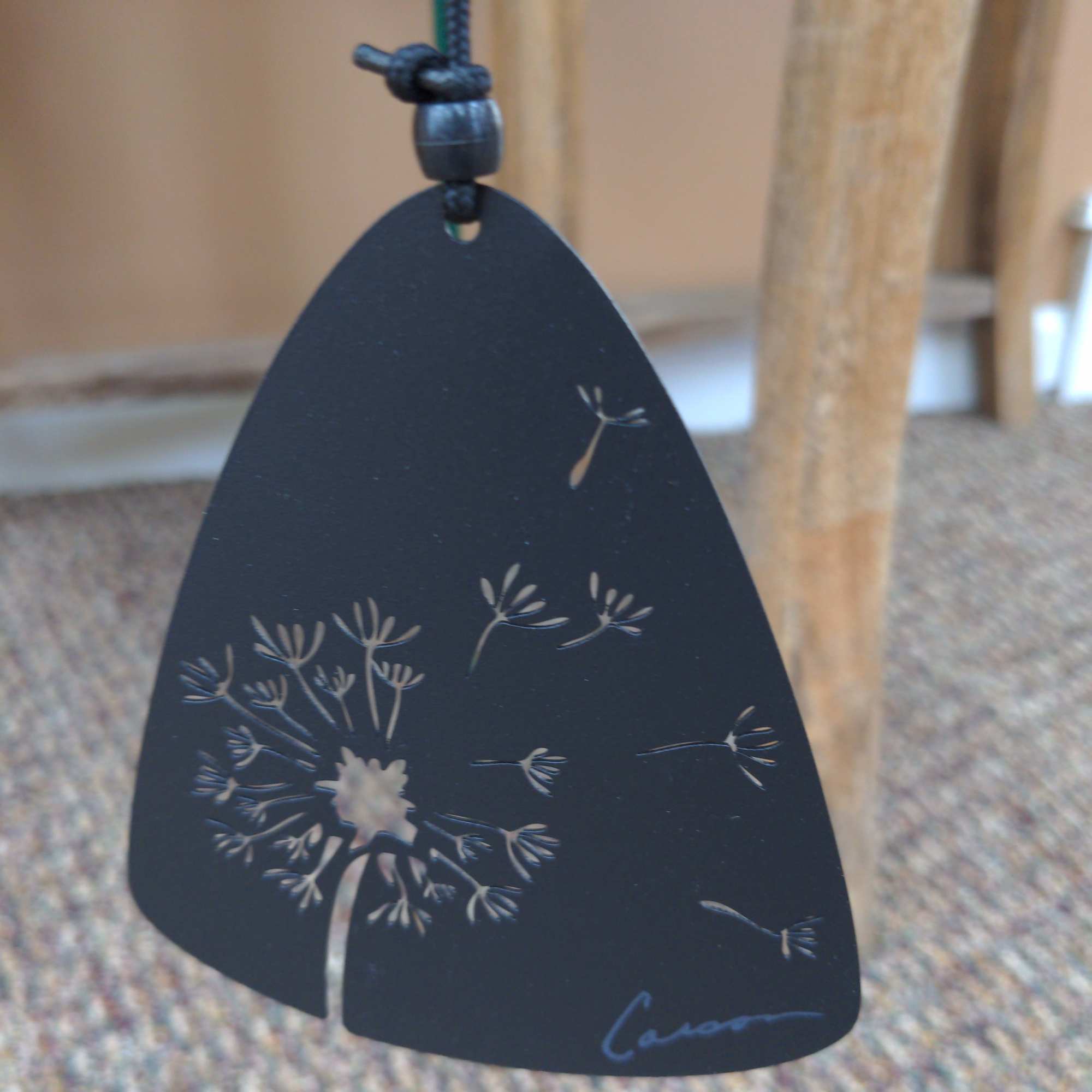 Black teardrop pendant with a white dandelion design on a cord