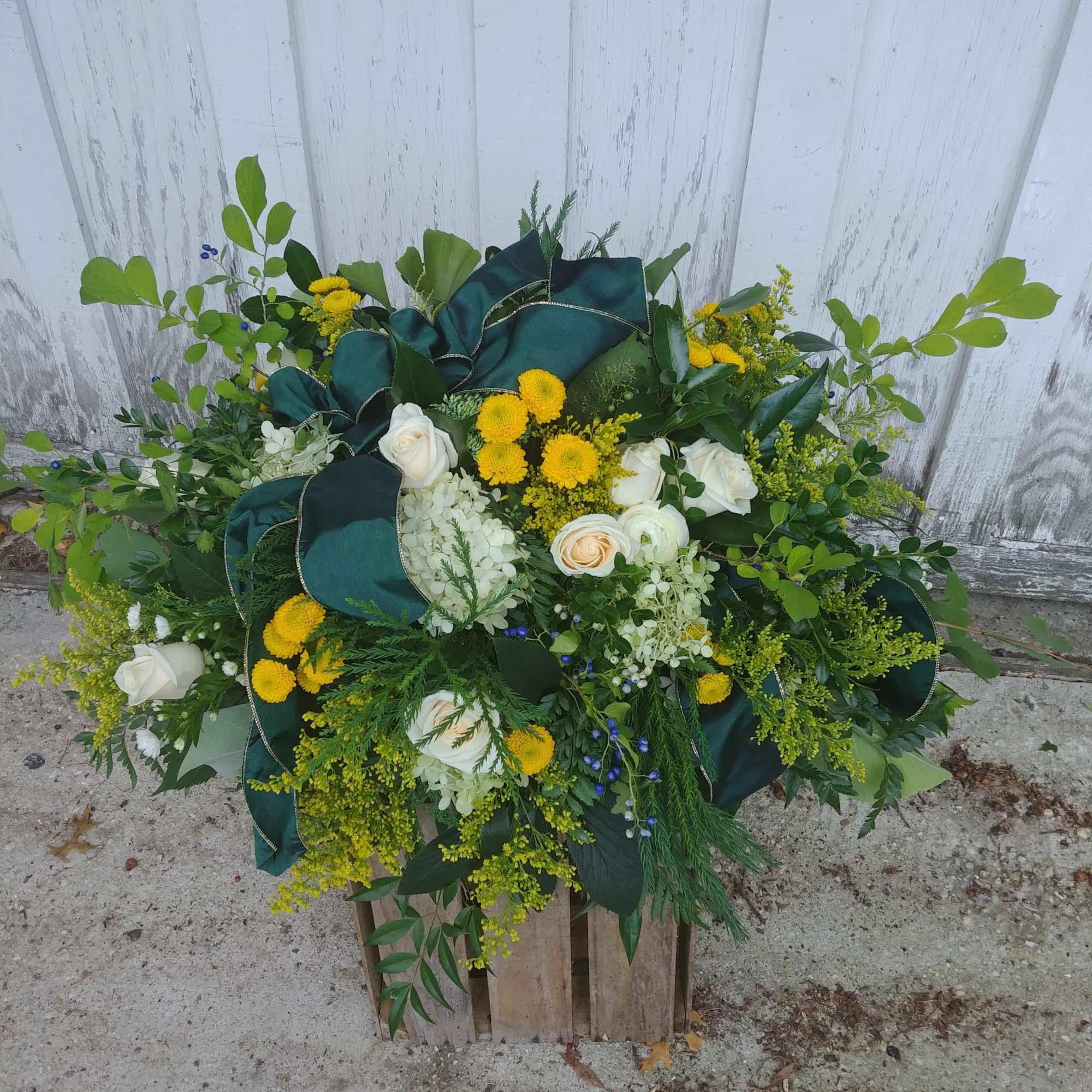 Large floral arrangement with white roses, yellow blooms, and dark green ribbon