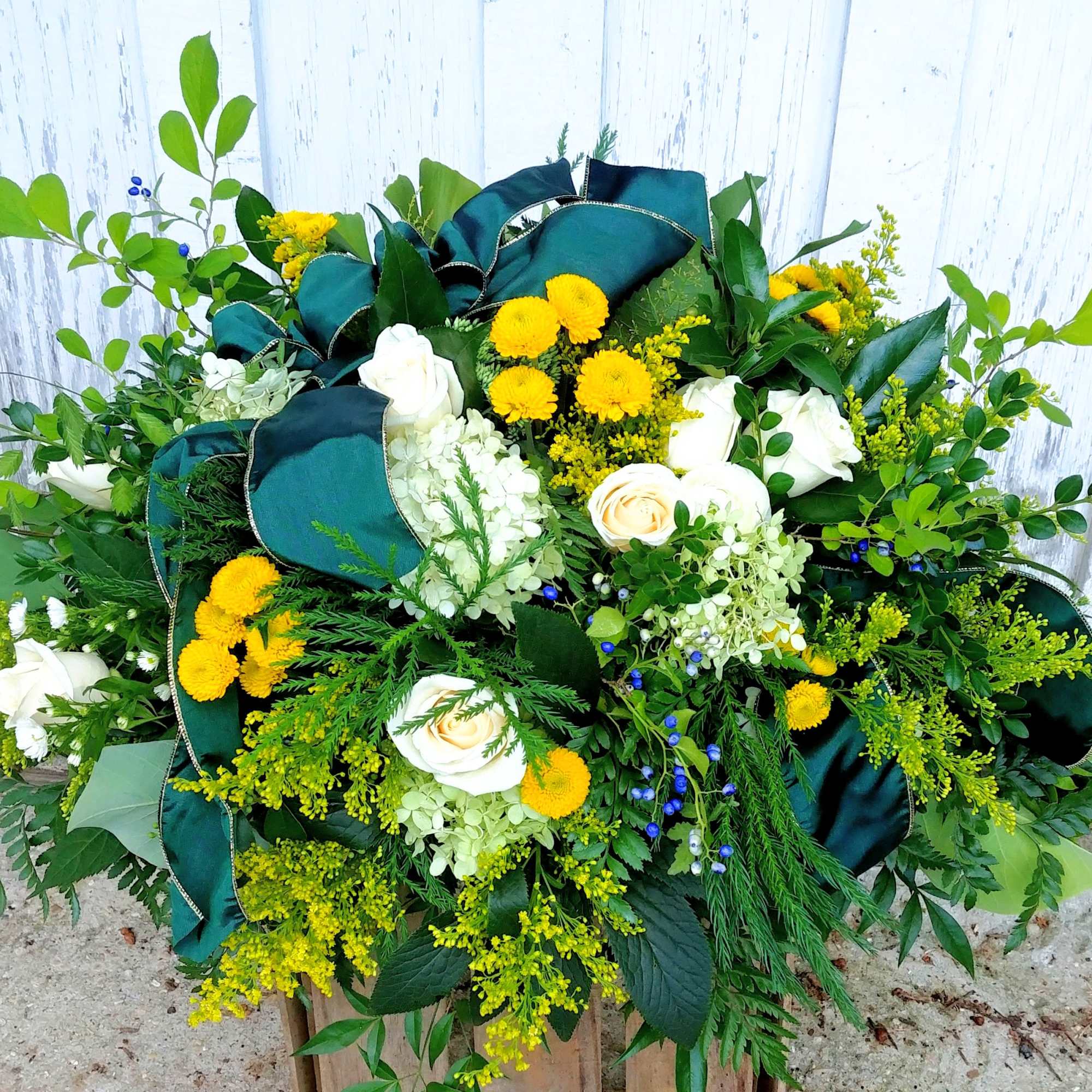 Large floral spray with white roses, yellow blooms, and dark green ribbon