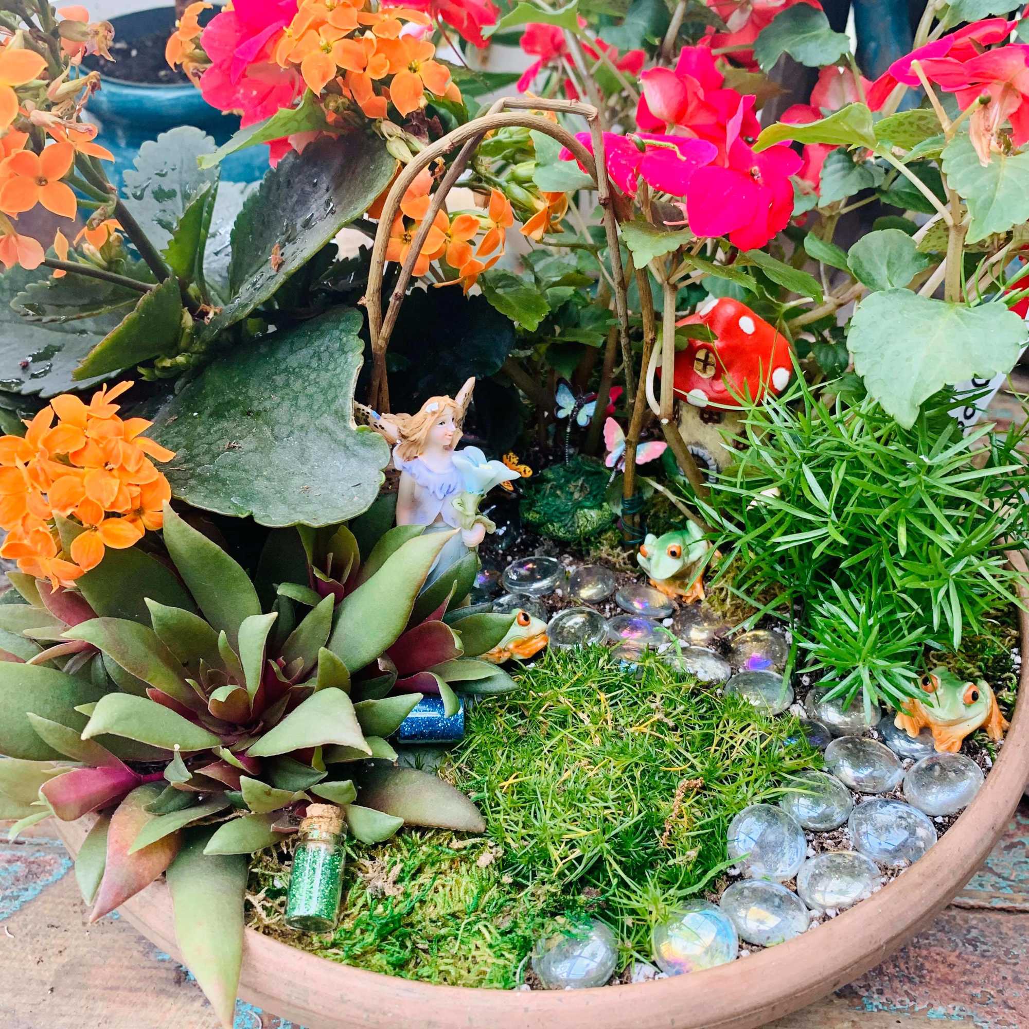 Potted succulent garden with bright pink and orange flowers and small fairy figurines