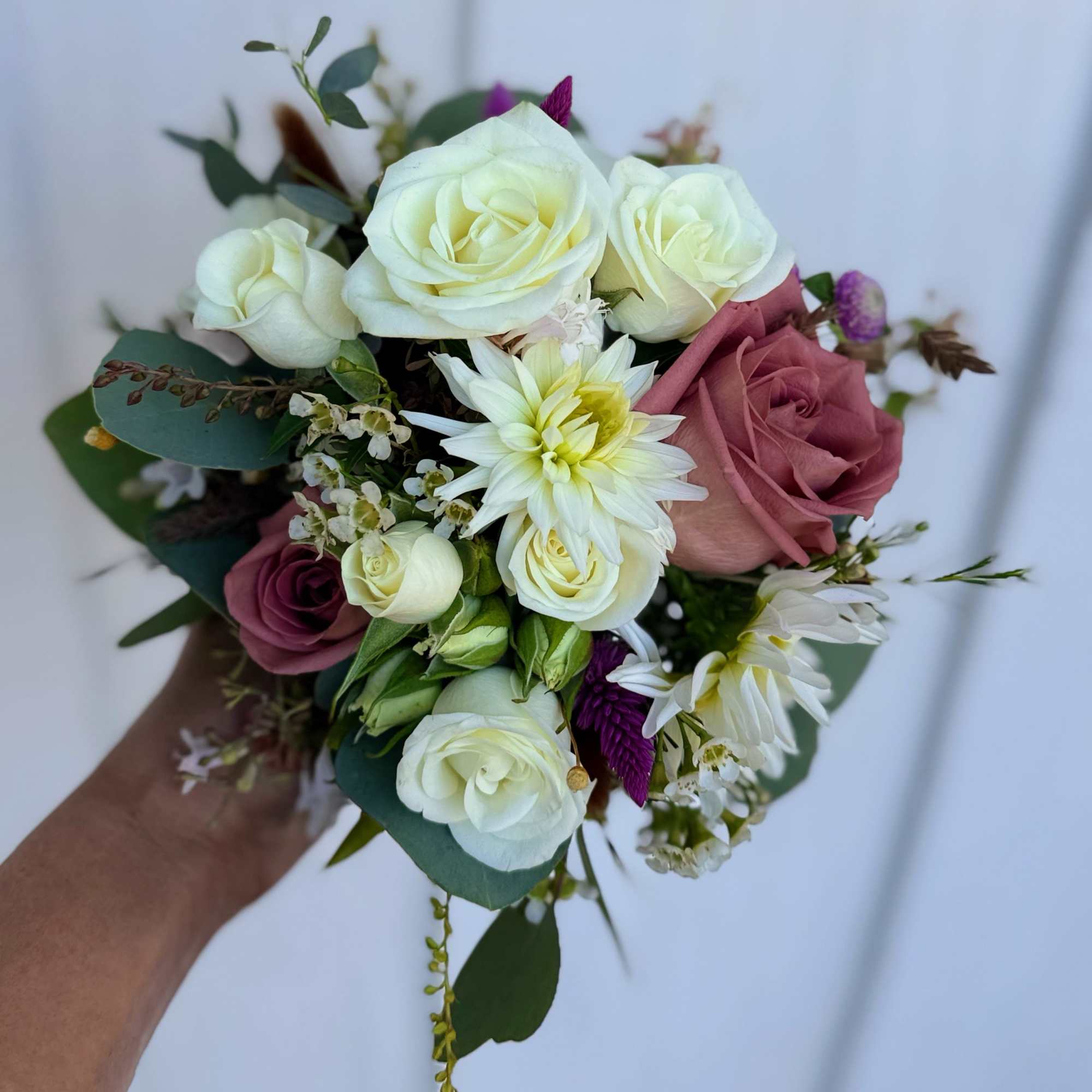 Handheld bouquet of white and mauve roses with white daisy-like blooms