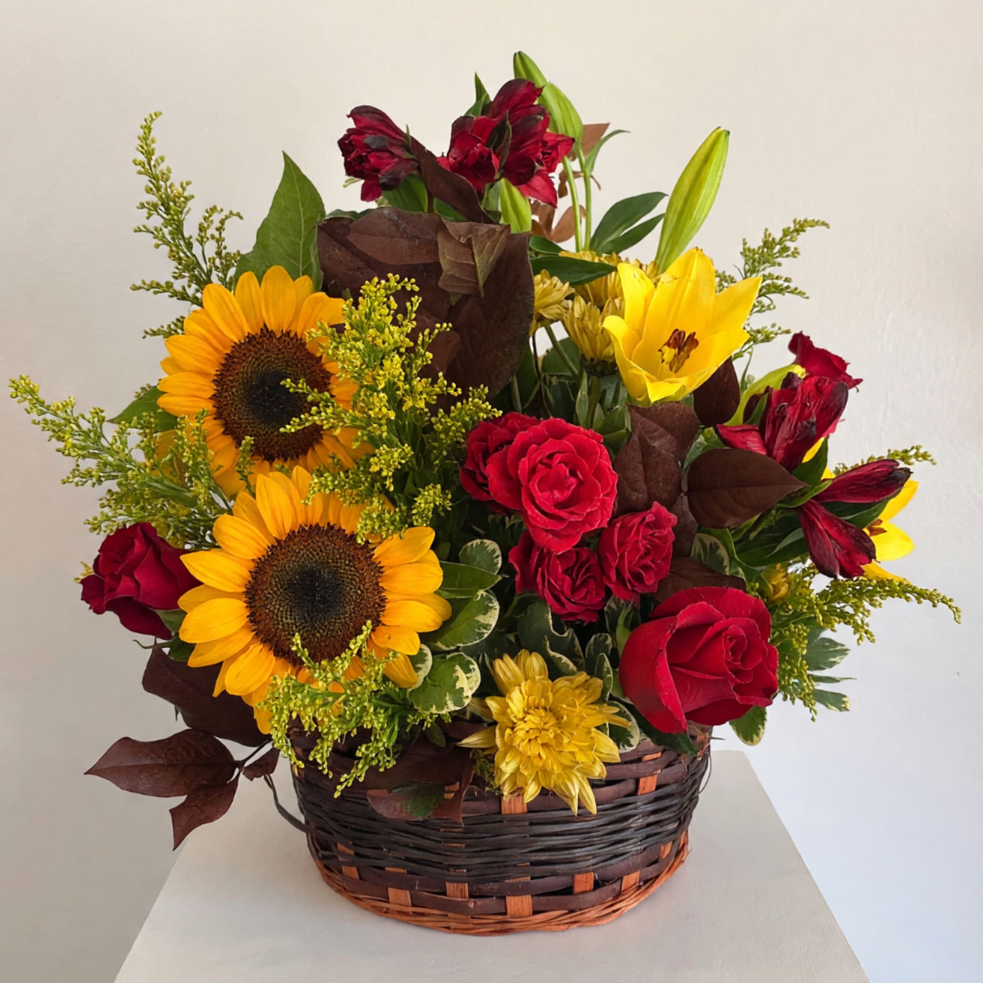 Basket arrangement with sunflowers, red roses, yellow lilies, and red alstroemeria