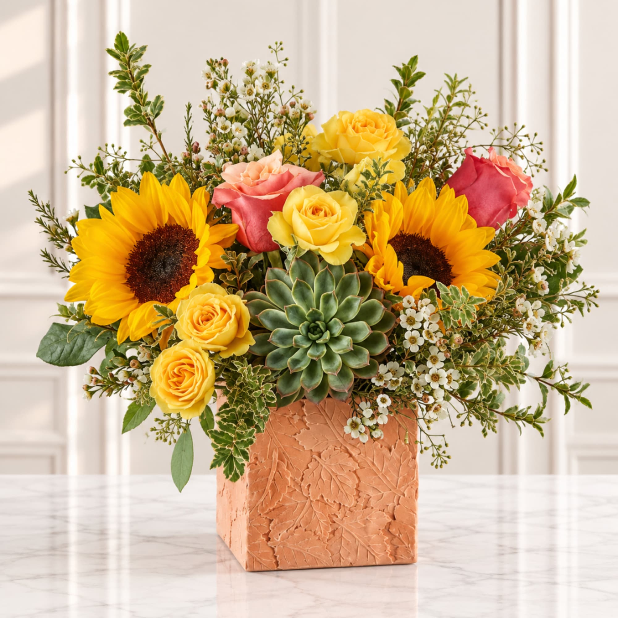 Sunflower and rose arrangement in a square peach vase with a succulent center