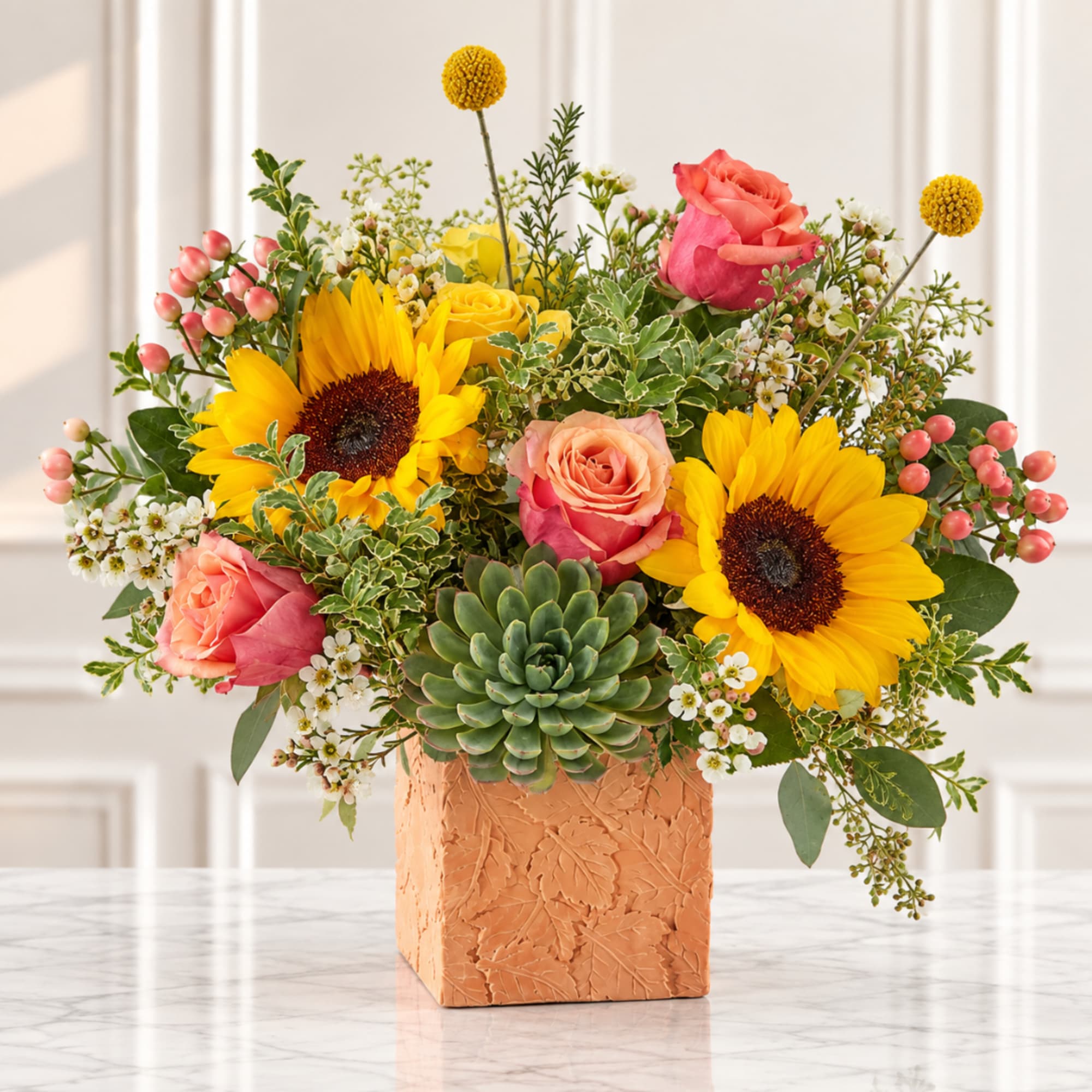 Sunflower and rose arrangement in a peach square vase with a succulent