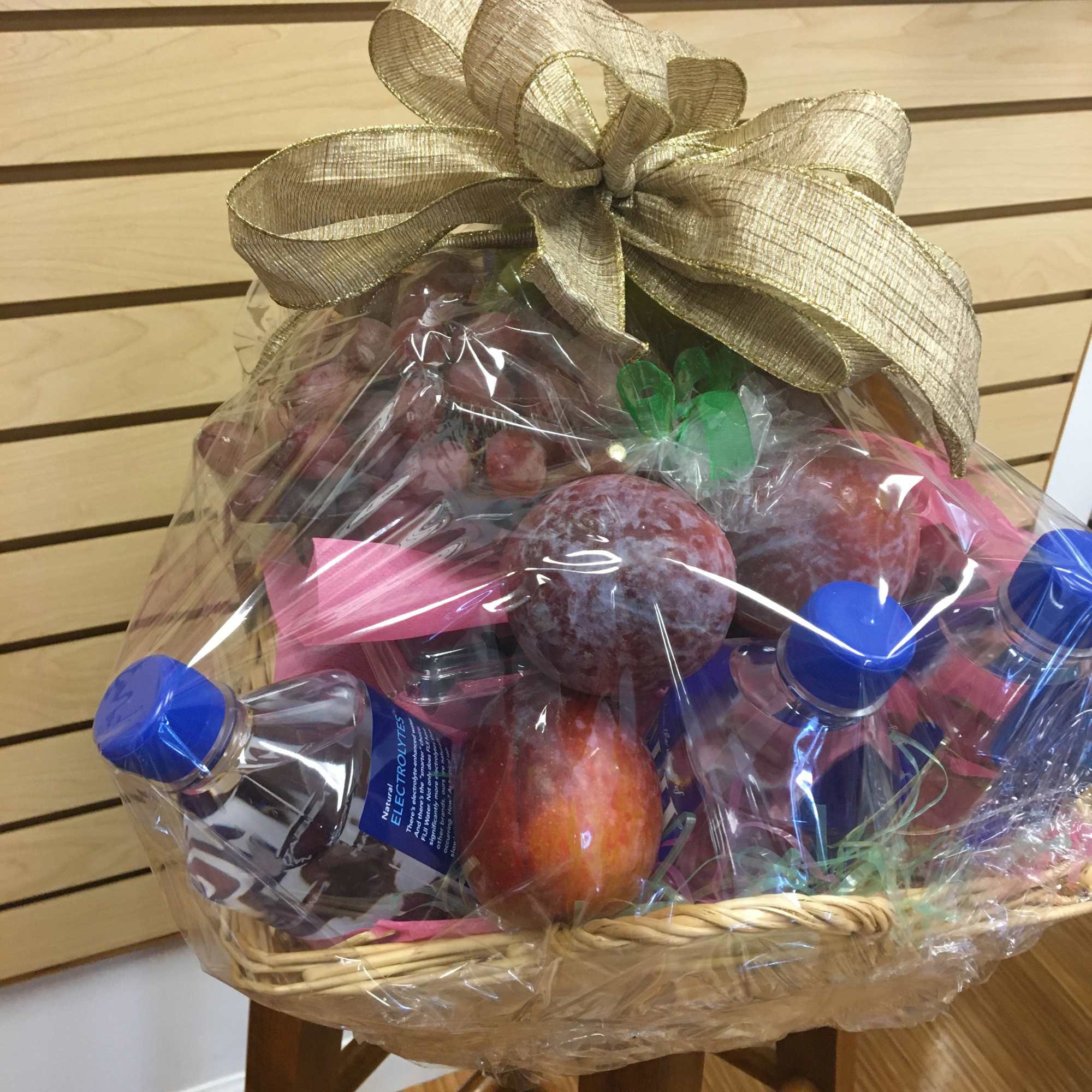 Gift basket with fruit and bottled drinks wrapped in clear plastic and topped with a gold bow