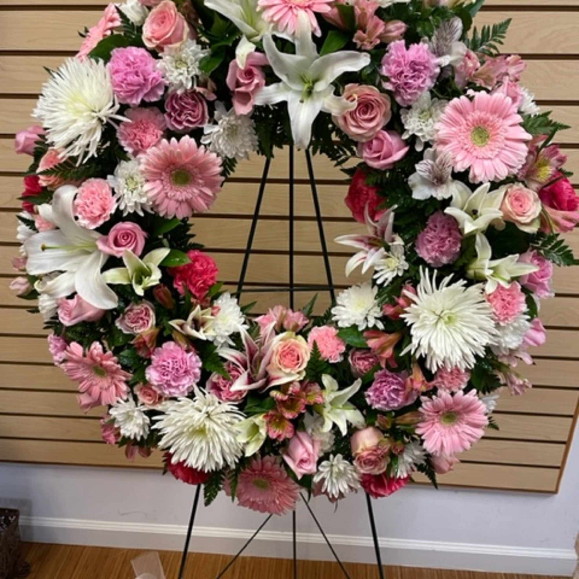Pink and white floral wreath on a black stand